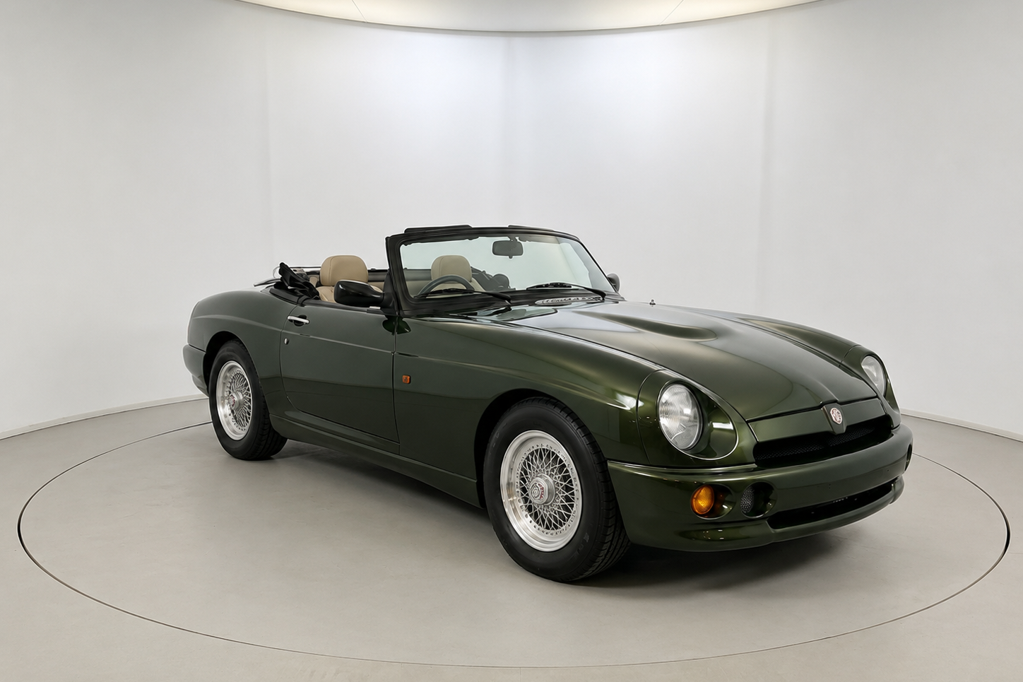 Dark metallic green MG RV8 roadster with the hood down, front three-quarter view on a studio turntable, showing the cream leather interior, body-colour bumpers, lattice alloy wheels and the smoothed MGB-derived body.