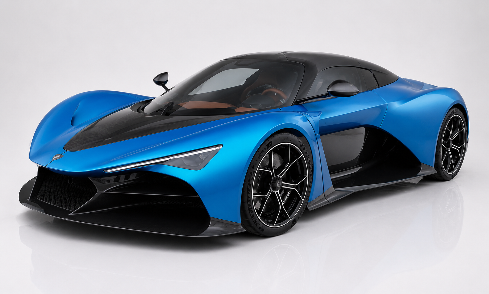Blue Zenvo Aurora hybrid hypercar in a studio setting, front three-quarter view showing the low mid-engine silhouette, exposed carbon-fibre roof panel and side vents, aggressive front splitter and multi-spoke black alloy wheels.