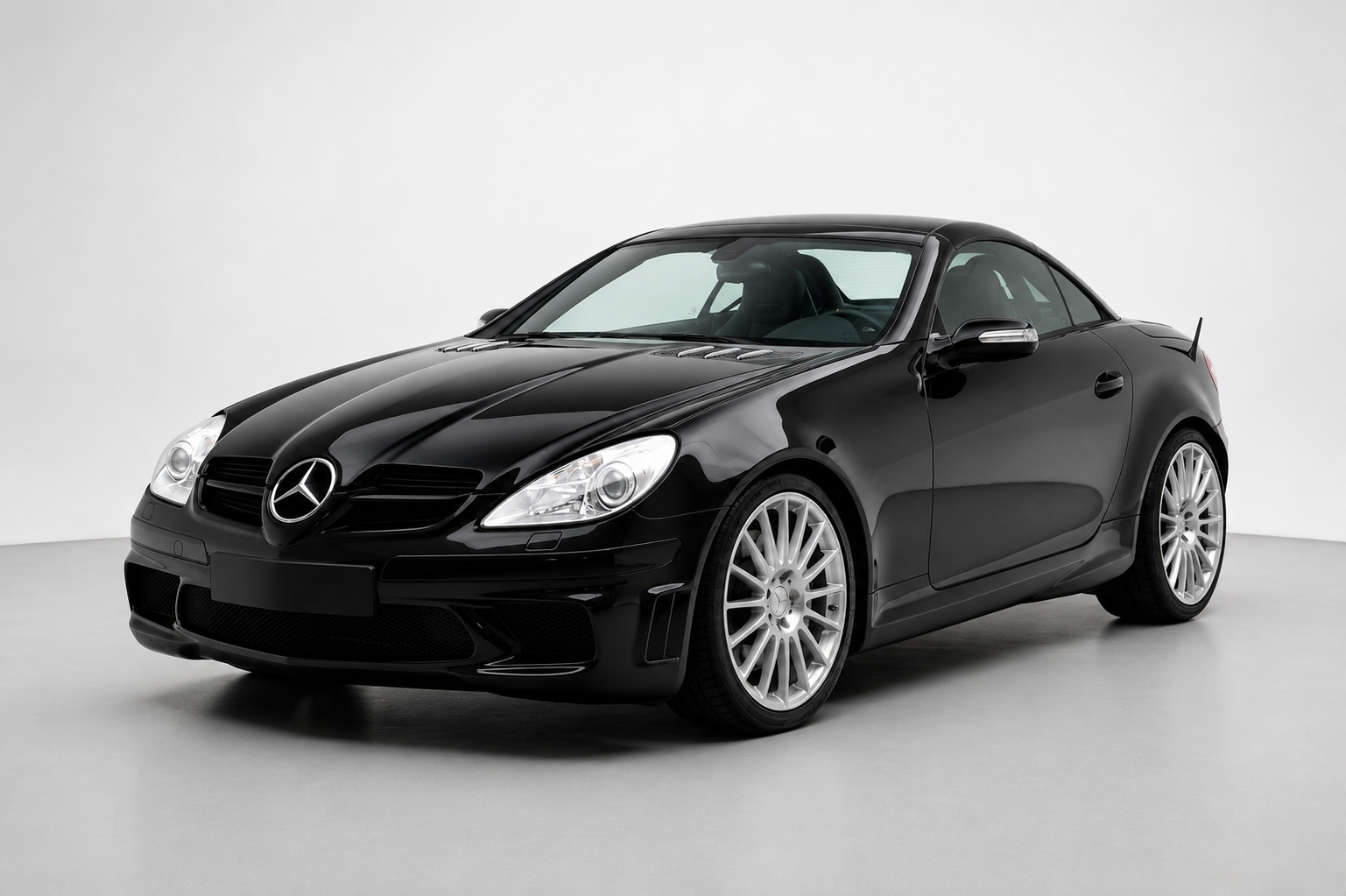 Black Mercedes-Benz SLK 55 AMG Black Series (R171) in a studio, front three-quarter view showing the fixed roof, bonnet vents, deep front bumper and silver multi-spoke AMG wheels.