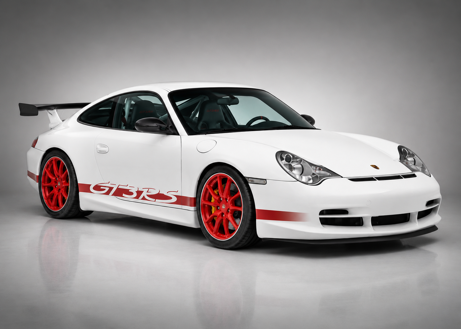 White Porsche 911 GT3 RS (996) in a studio setting, front three-quarter view showing the red side script, red centre-lock-style alloy wheels and fixed carbon rear wing.