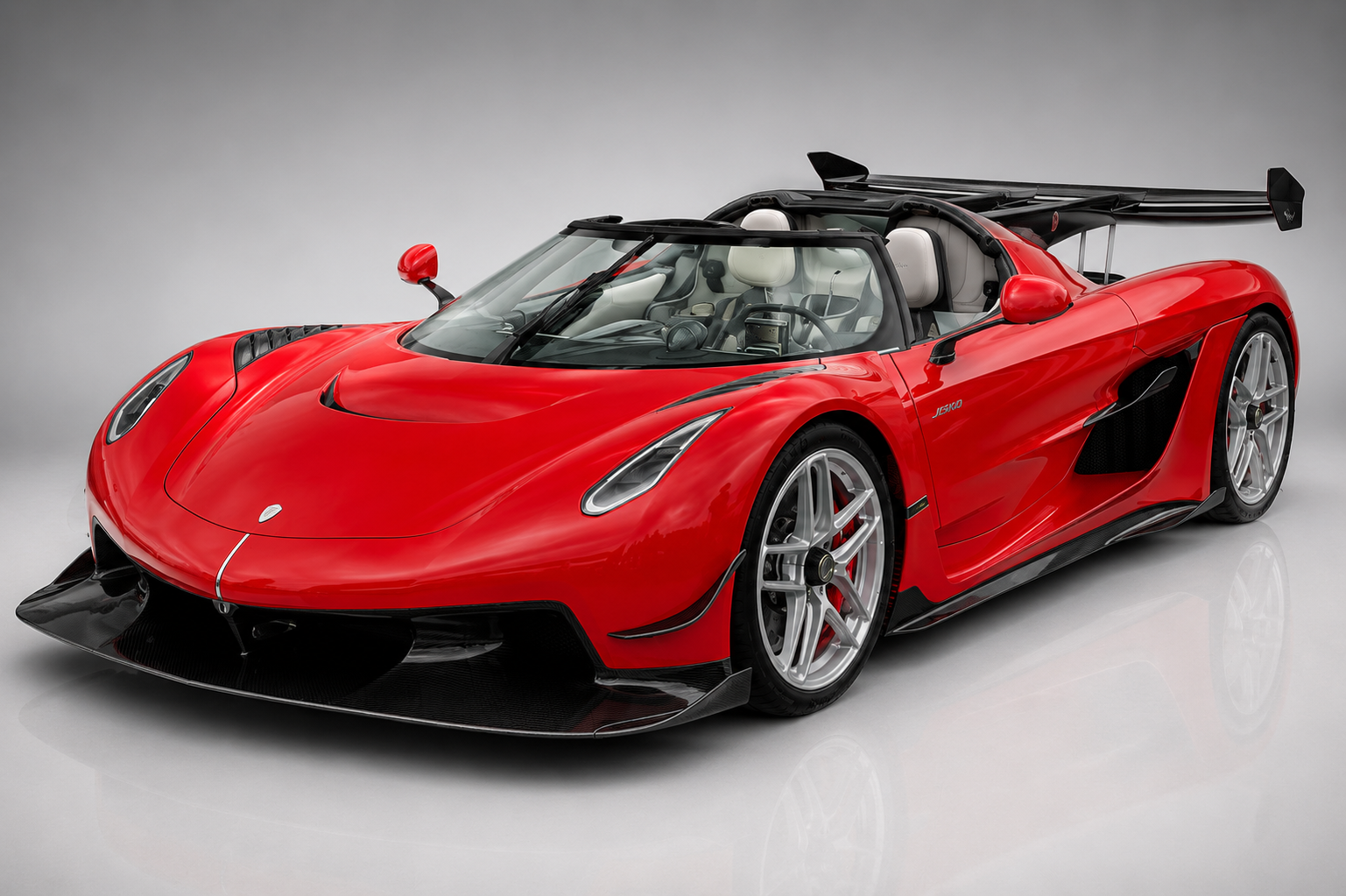 Red Koenigsegg Jesko hypercar in a studio setting, front three-quarter view showing the open targa roof, aggressive front splitter and canards, distinctive headlamps, large carbon-fibre side intakes, multi-spoke alloy wheels and the extreme aero-focused hypercar proportions.
