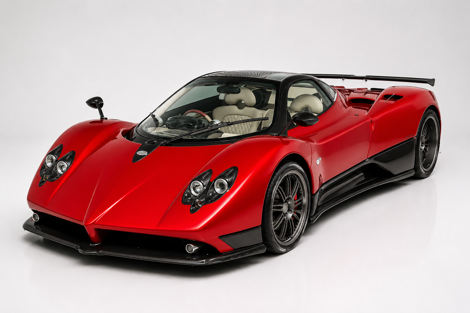Red Pagani Zonda F in a studio setting, front three-quarter view showing the flowing carbon-fibre bodywork, quad-round LED headlight clusters, low front splitter and multi-spoke wheels.