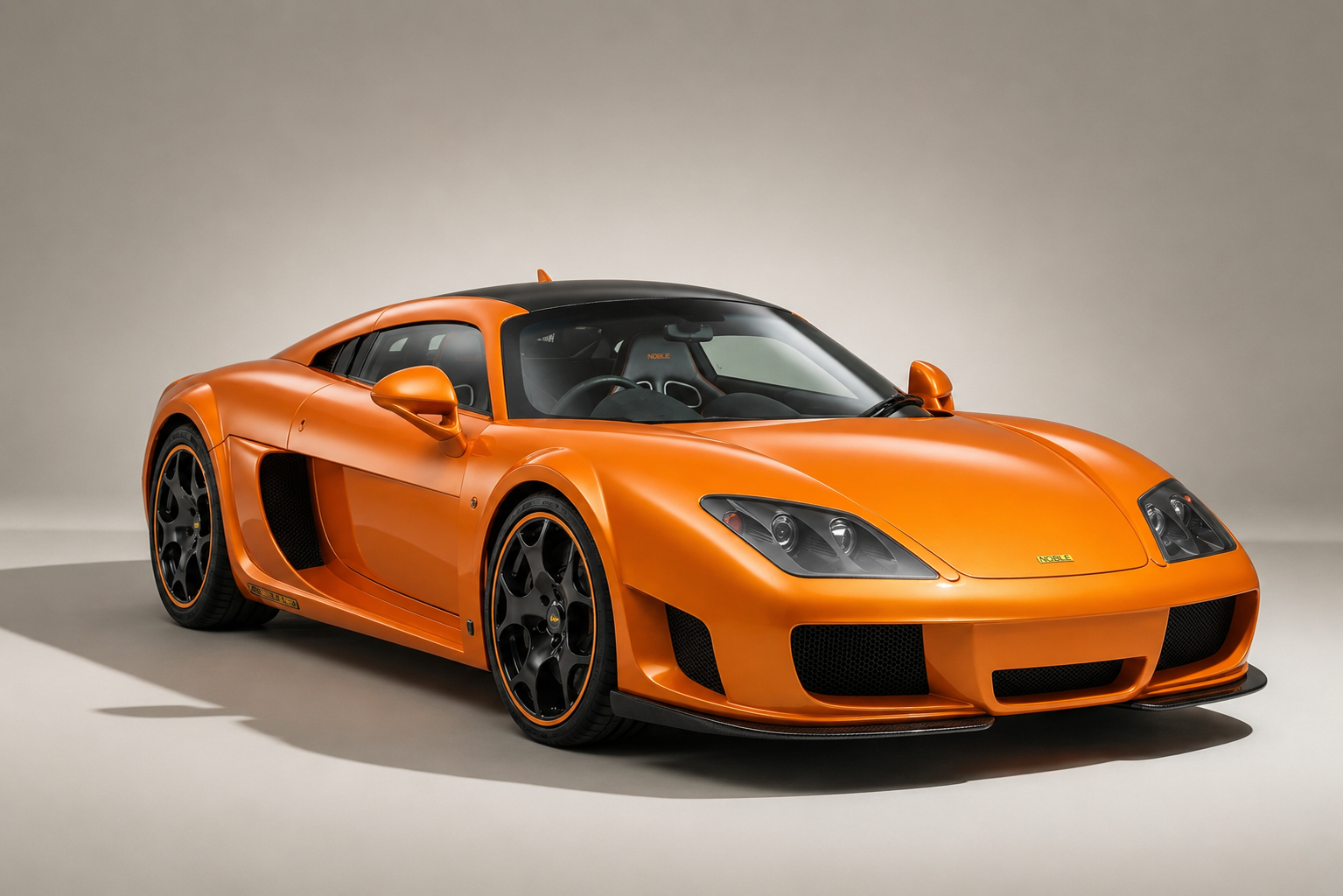 Orange Noble M600 Carbon Sport in a studio, front three-quarter view showing the black carbon-fibre roof, twin-lens headlamps, Noble badge on the nose, front splitter and black wheels with orange rim accents.