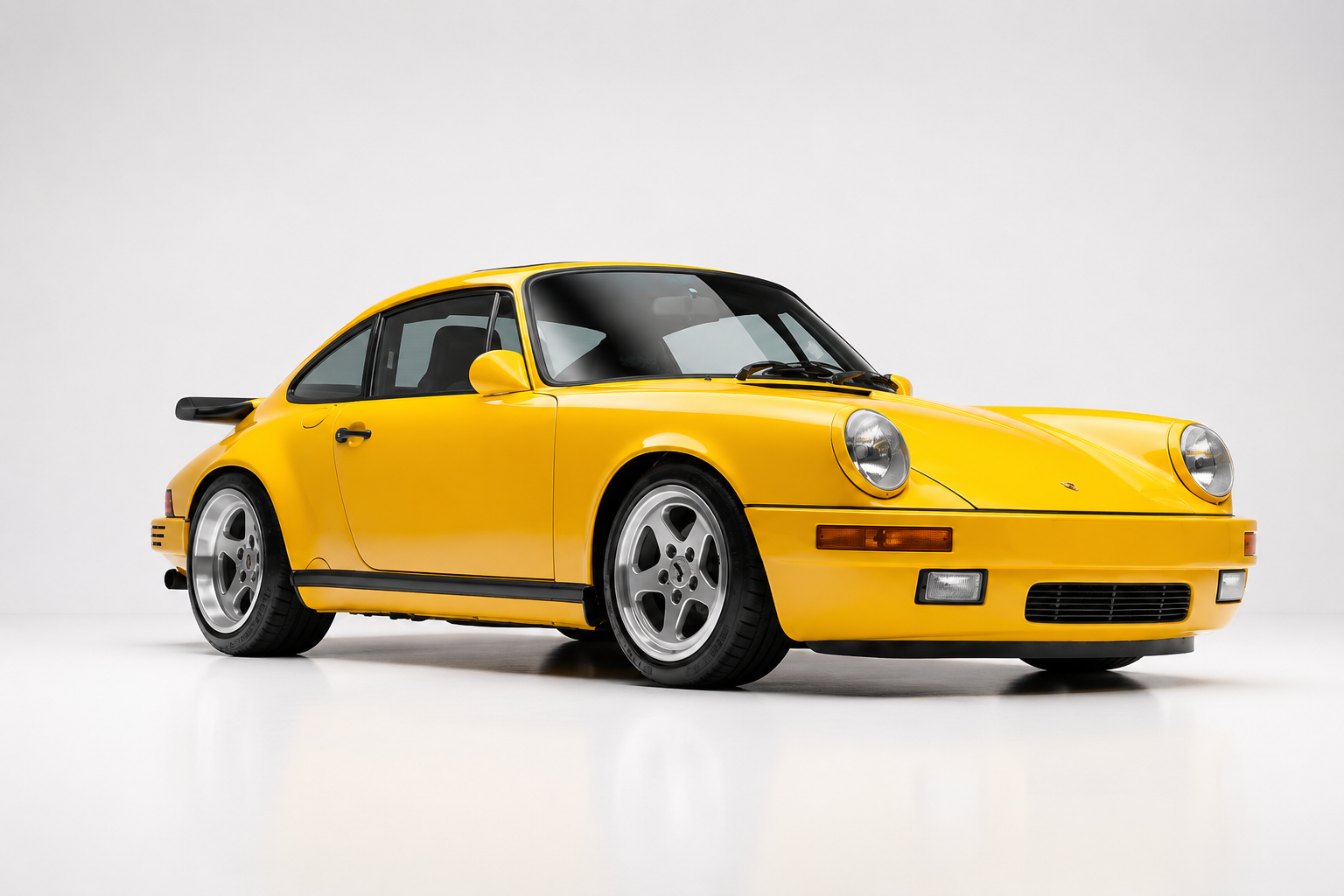 Blossom Yellow RUF CTR 'Yellowbird' in a studio setting, front three-quarter view showing the narrow-body 911 Carrera 3.2 silhouette, classic round headlamps, RUF five-spoke wheels and subtle rear spoiler — the 1987 Road & Track world's-fastest test winner.
