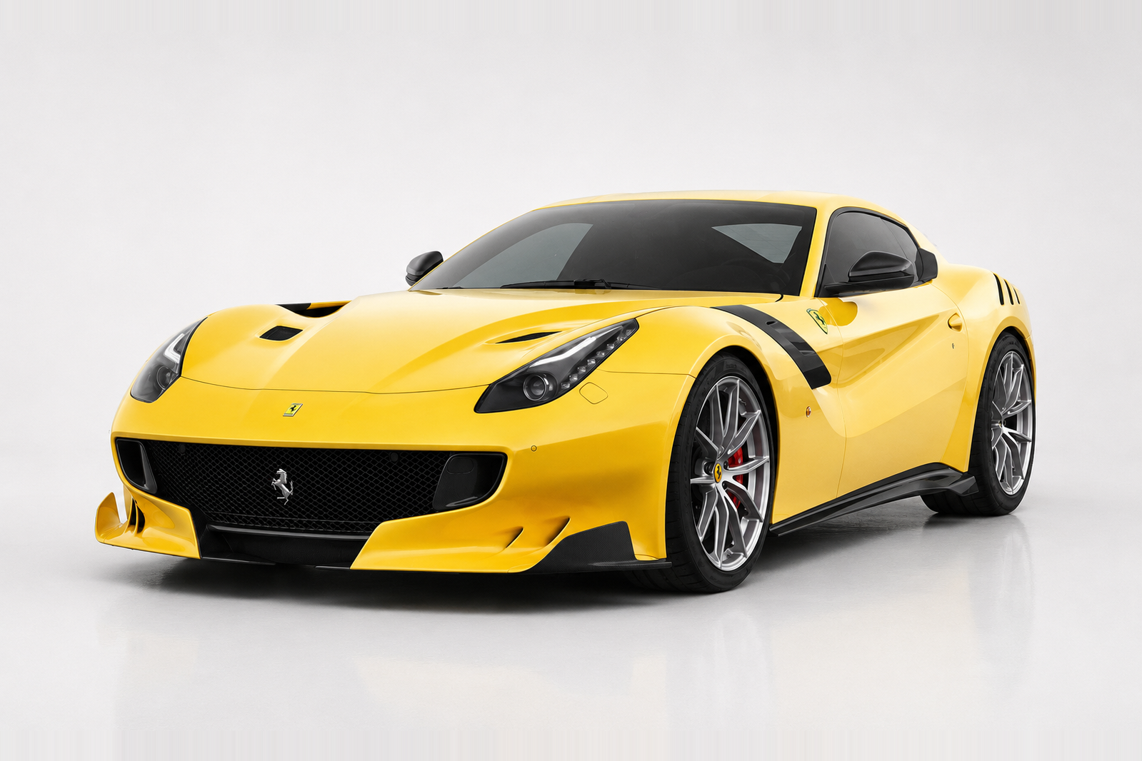 Yellow Ferrari F12tdf photographed in a studio, front three-quarter view showing the deep front splitter with aero flaps, bonnet louvres, black wheel-arch extensions, forged multi-spoke wheels and carbon-ceramic brakes.