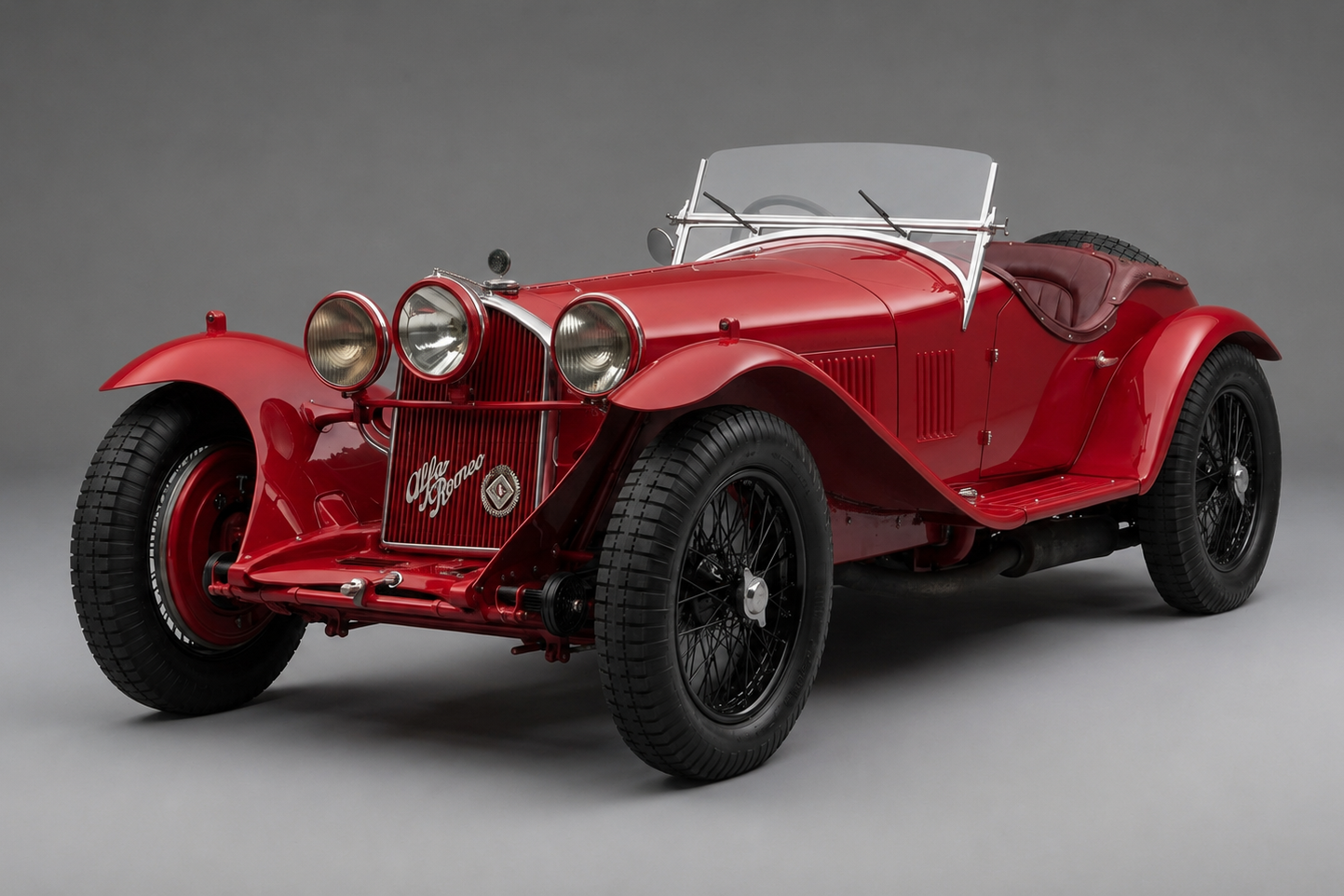 Red Alfa Romeo 8C 2300 open two-seater sports car, front three-quarter studio view, showing the tall chrome grille with 'Alfa Romeo' script, triple headlights, folded aero screen and black wire wheels.