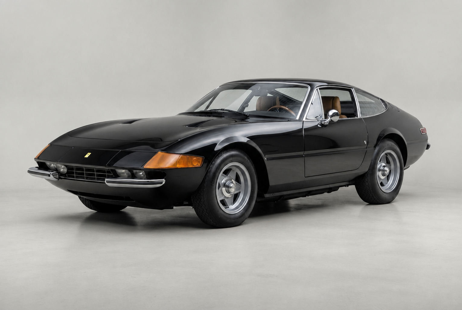 Black Ferrari 365 GTB/4 Daytona, front three-quarter studio view on a pale grey backdrop, showing the early plexiglass full-width headlamp panel, amber indicators, five-spoke alloy wheels with three-eared knock-offs, chrome door mirror and tan leather interior.