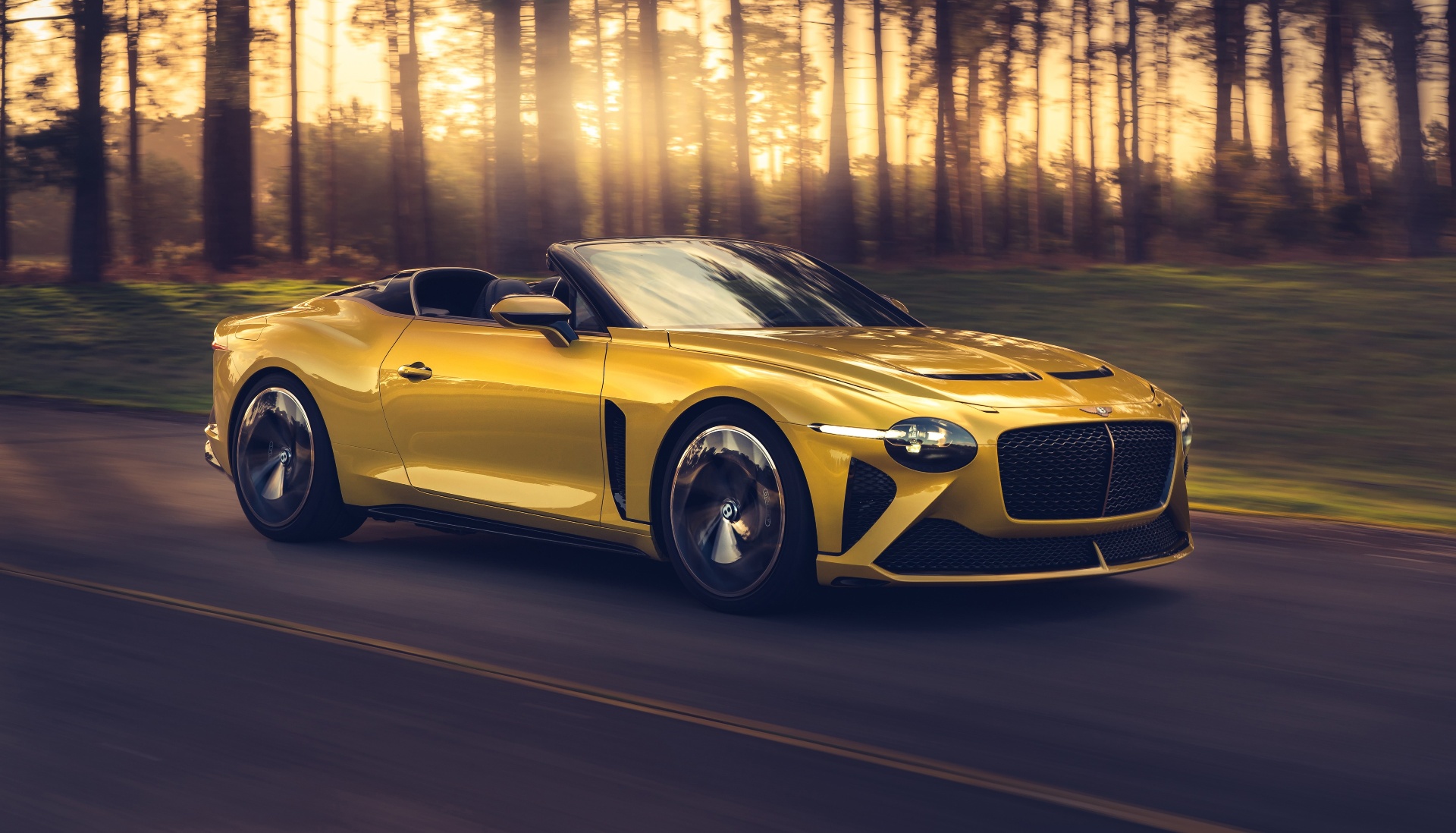 Yellow Bentley Mulliner Bacalar in front three-quarter view, photographed at golden hour with sunlit pine forest behind — user-supplied Bentley press image. Flagged for review: this is a factory press motion shot on a road rather than a static concours/estate/showroom setting per the standing hero-image brief.
