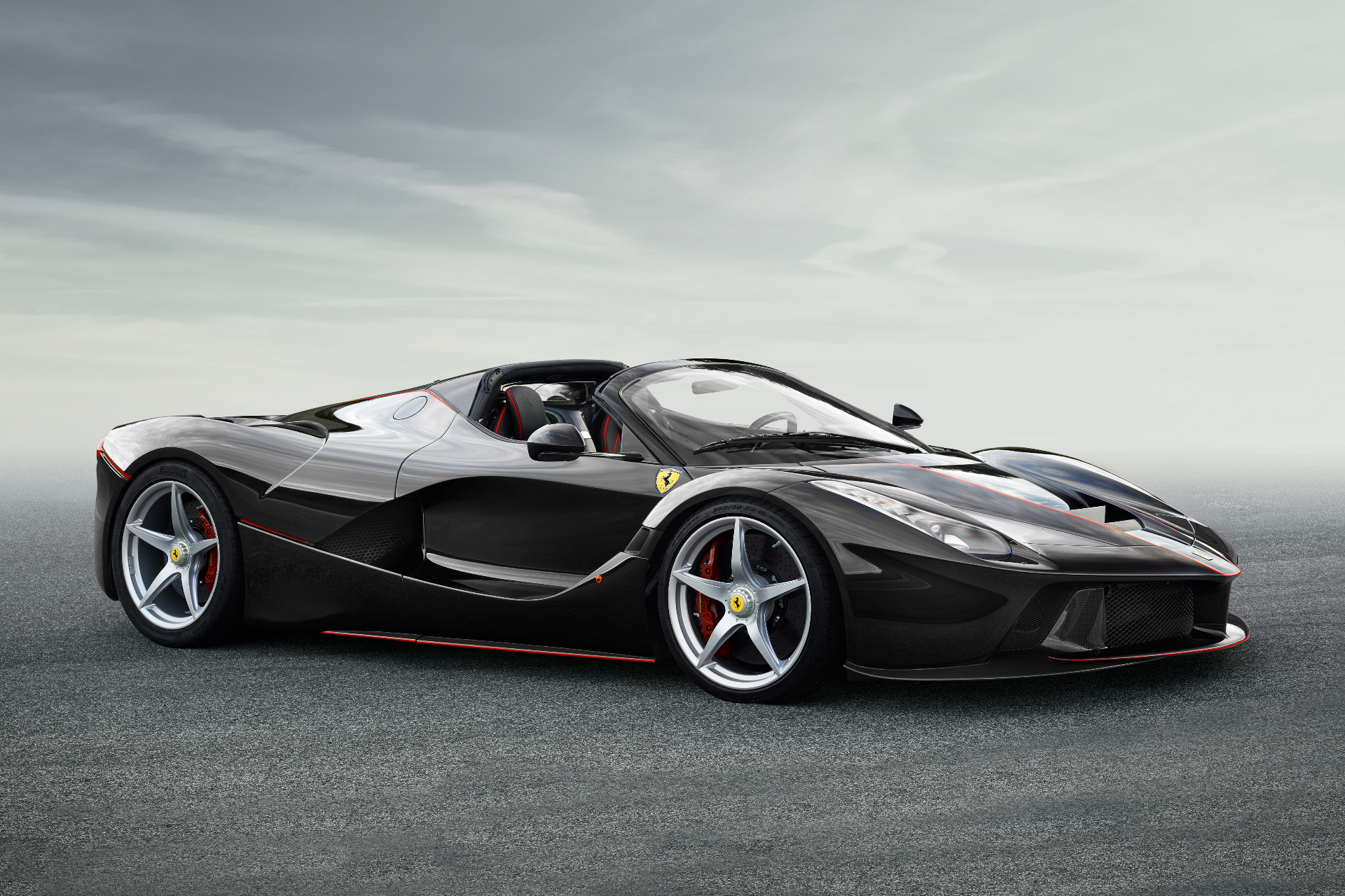 Black Ferrari LaFerrari Aperta with open roof and red pinstripe accents, front three-quarter studio view on tarmac against a grey sky, showing the sculpted carbon-fibre bodywork, silver five-spoke wheels and red brake calipers.