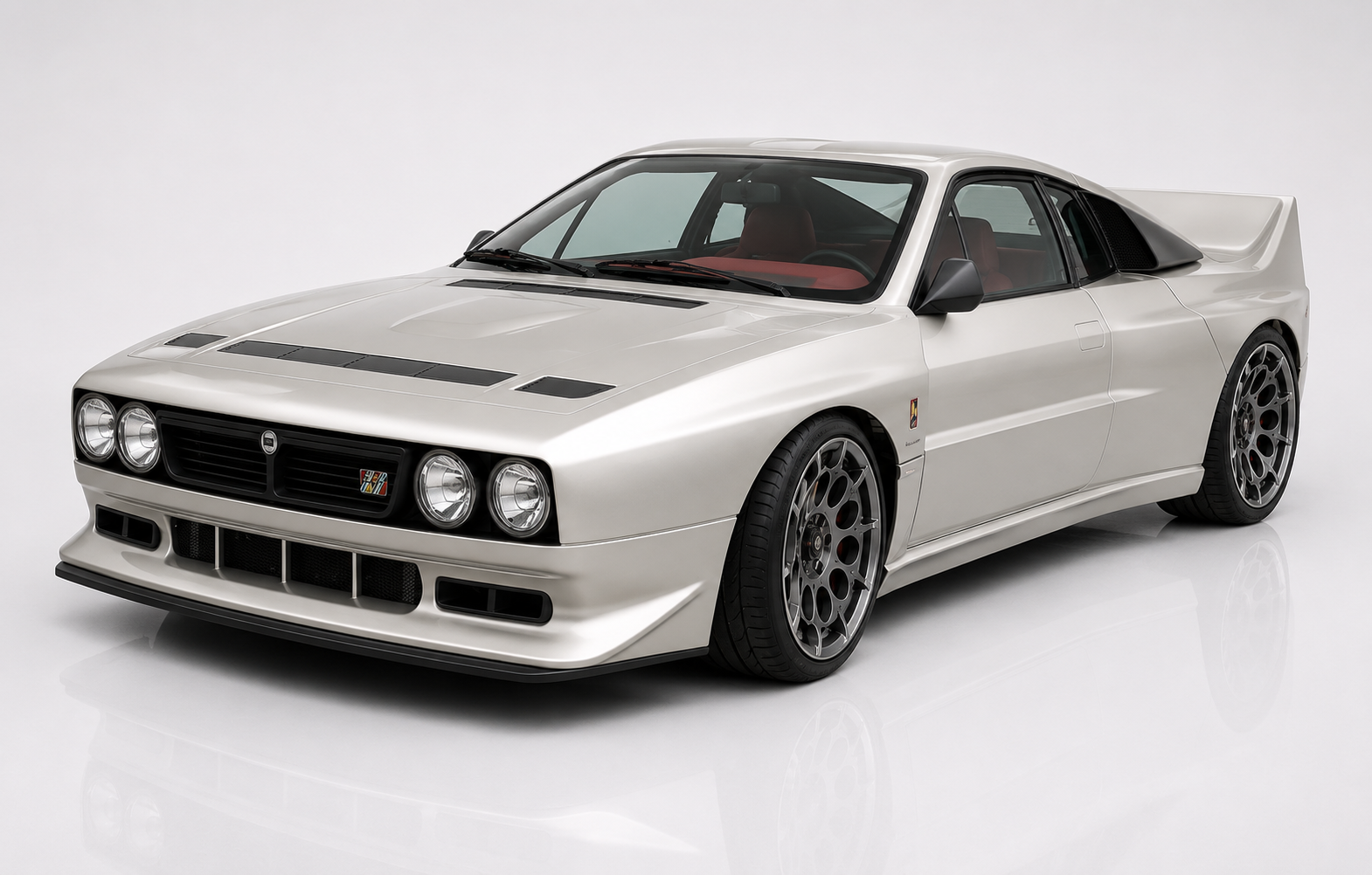Silver Kimera Evo37 in a studio setting, front three-quarter view showing the Lancia 037-inspired silhouette with quad round headlamps, deep front splitter, factory bonnet vents, integrated side sills and multi-spoke Speedline-style wheels — the RWD restomod tribute to Lancia's last RWD WRC champion.