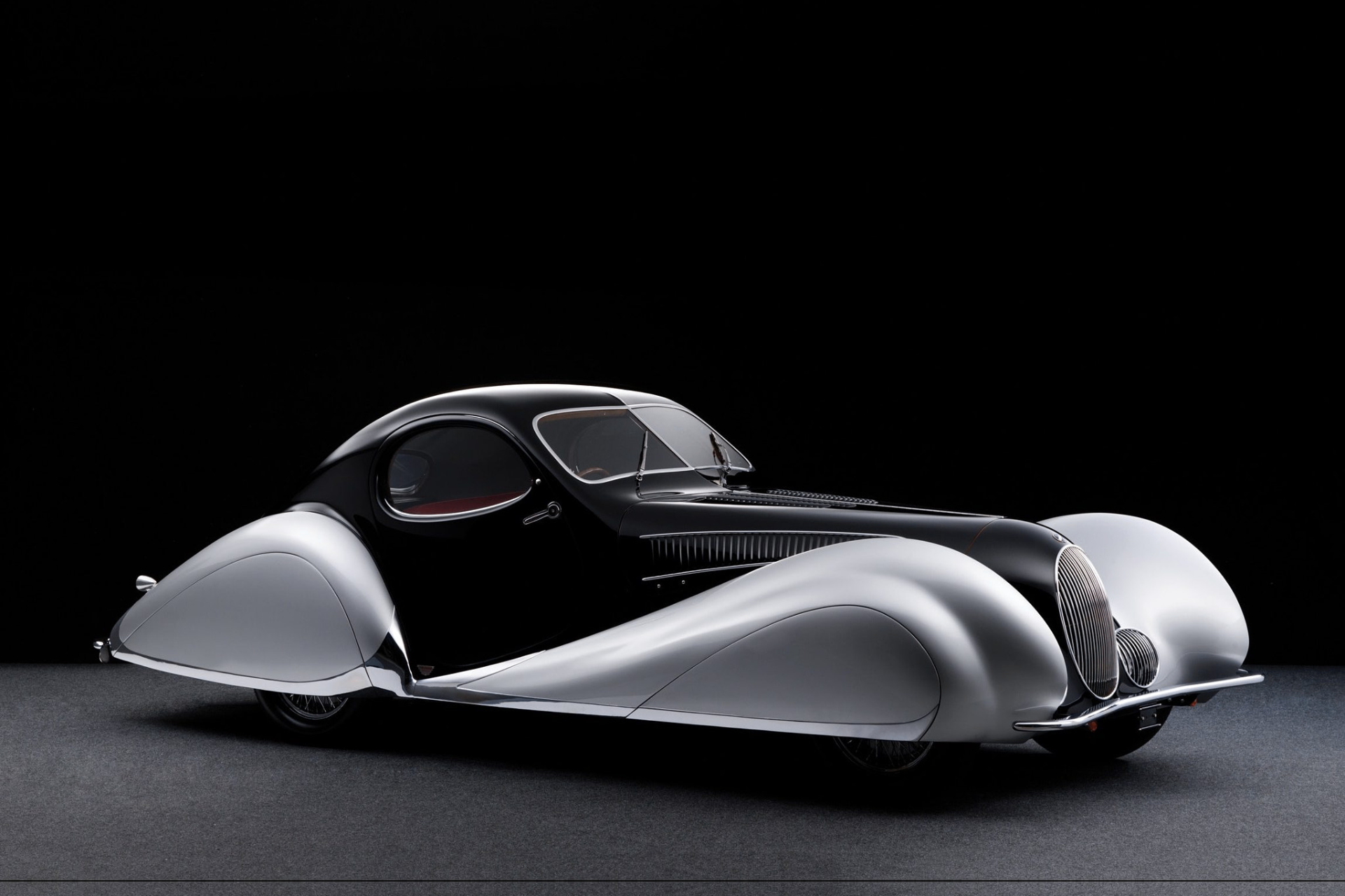 Silver and black Talbot-Lago T150-C SS Teardrop coupe, side three-quarter studio view on a black backdrop showing the sweeping streamlined 'Goutte d'Eau' bodywork, faired-in front wings, teardrop rear haunches and vertical chrome grille.