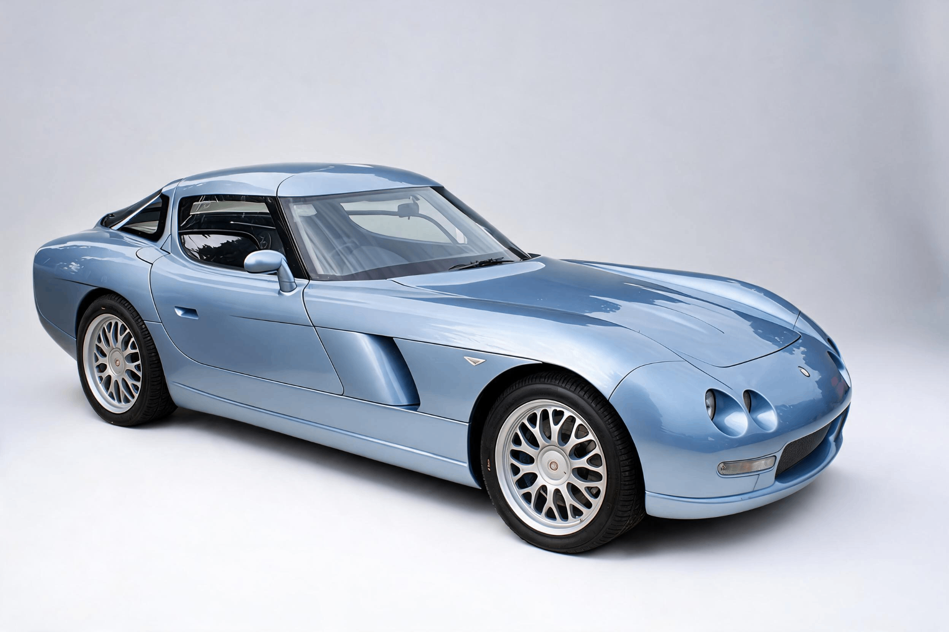Light blue Bristol Fighter coupé, front three-quarter studio view, showing the smooth aerodynamic body, a raised gullwing door and twin bonnet nostrils.