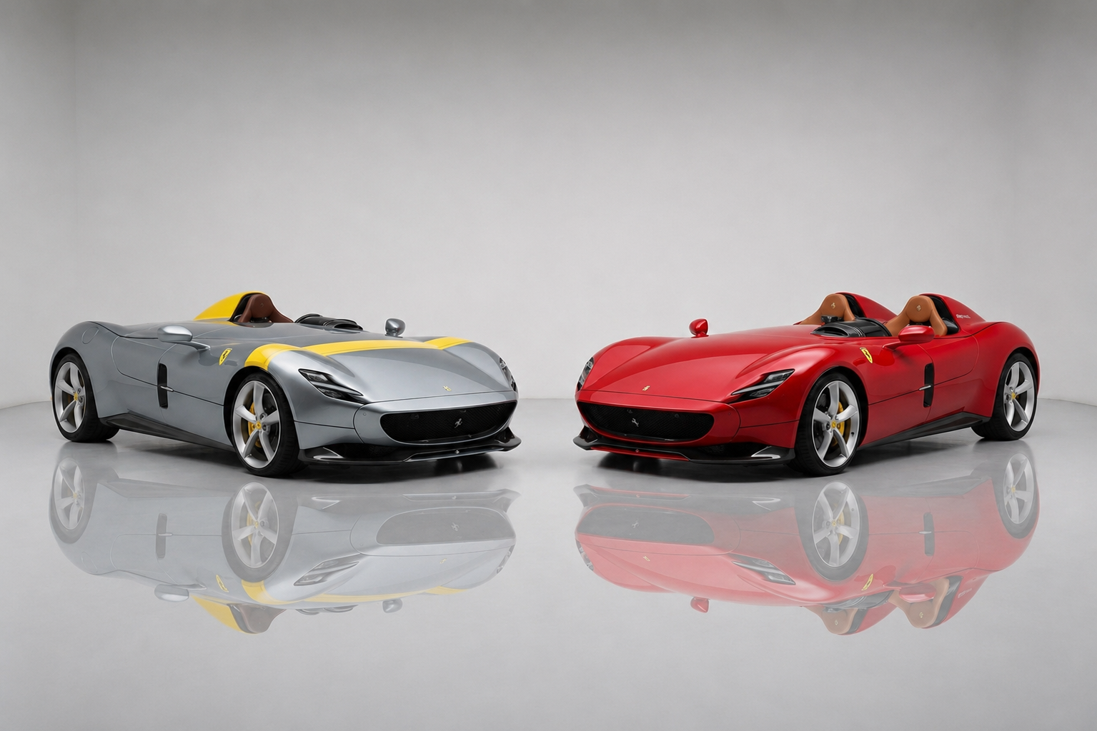 Ferrari Monza SP1 and SP2 Icona barchettas in a studio setting — a silver single-seater SP1 with a yellow centre stripe alongside a red two-seater SP2, both showing the open-cockpit V12 bodies, tan leather seats and multi-spoke alloy wheels.