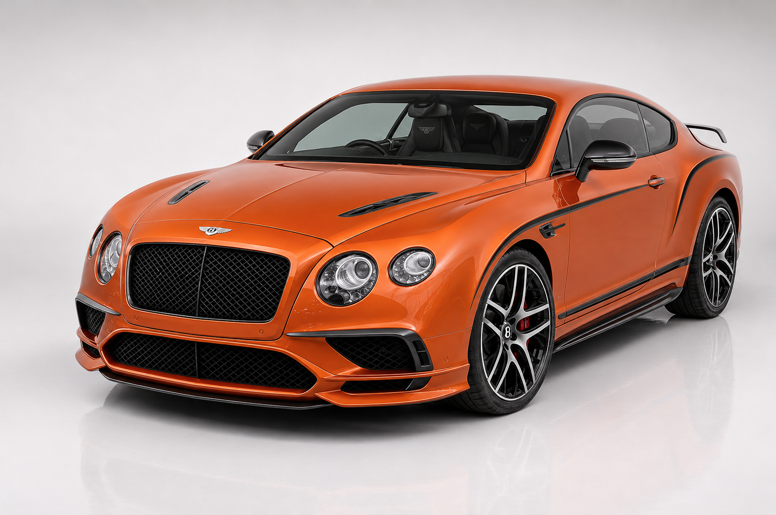 Orange Bentley Continental GT coupé in a bright studio, front three-quarter view showing the matrix grille with winged 'B' badge, quad round headlamps, vented bonnet, side vent behind the front wheel and multi-spoke dark alloy wheels with red brake calipers.