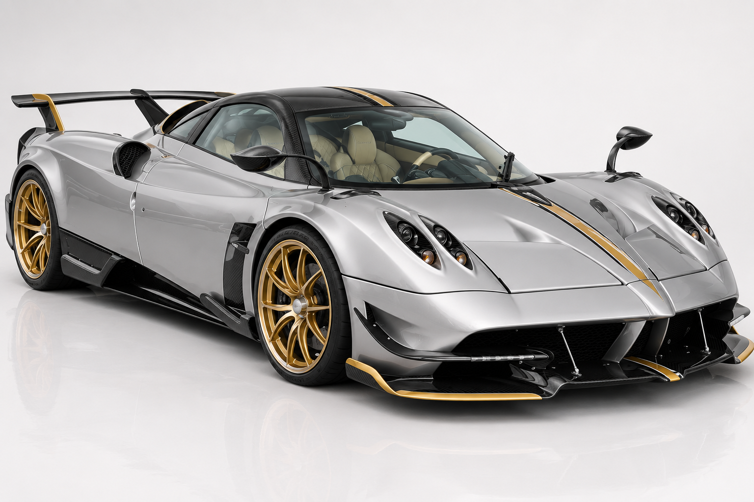 Silver Pagani Huayra BC with gold twin racing stripes and gold multi-spoke wheels in a studio setting, front three-quarter view showing the aggressive splitter, side intakes and low ride height.