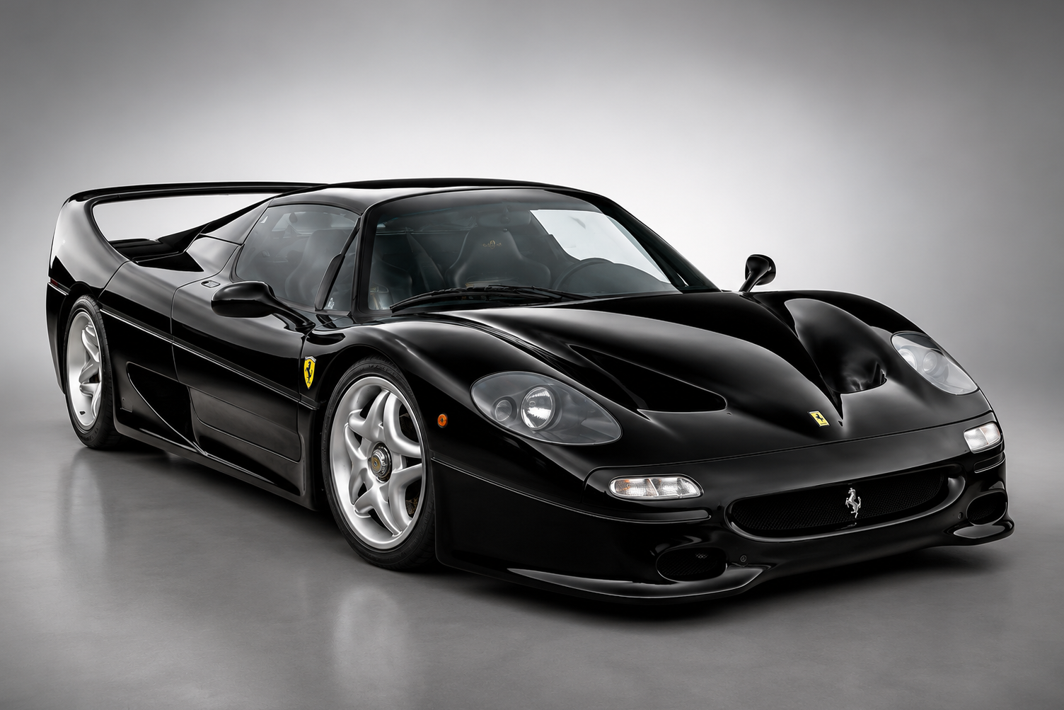 Black Ferrari F50 supercar in a studio setting, showing the low-slung Pininfarina bodywork, silver five-spoke wheels and rear spoiler.