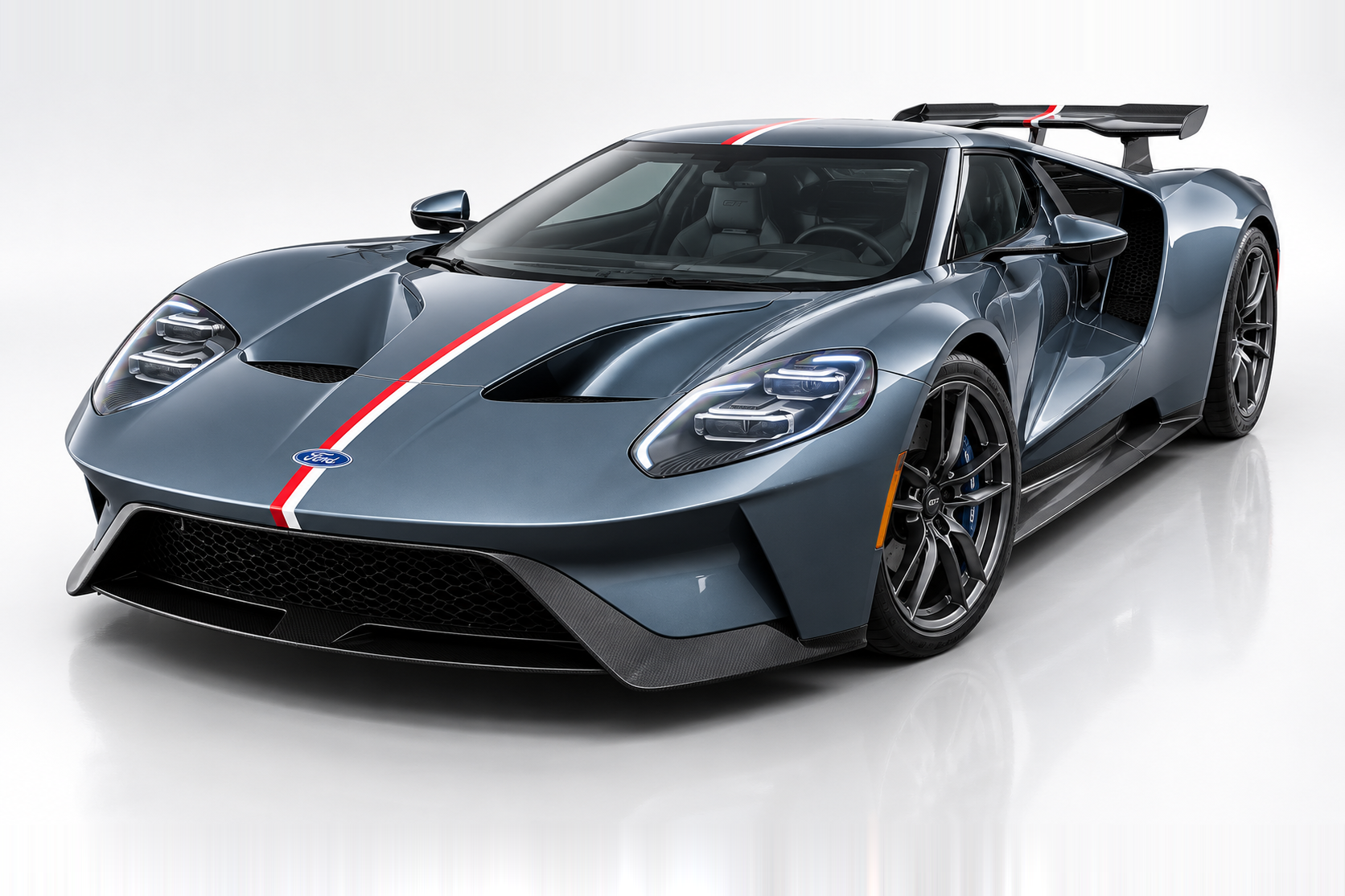 Dark grey Ford GT (2017–2022) photographed in a studio with red-and-white centre stripe, front three-quarter view showing the low nose, twin round headlamps with LED signature, flying-buttress rear, large rear wing, blue-caliper brakes and multi-spoke wheels.