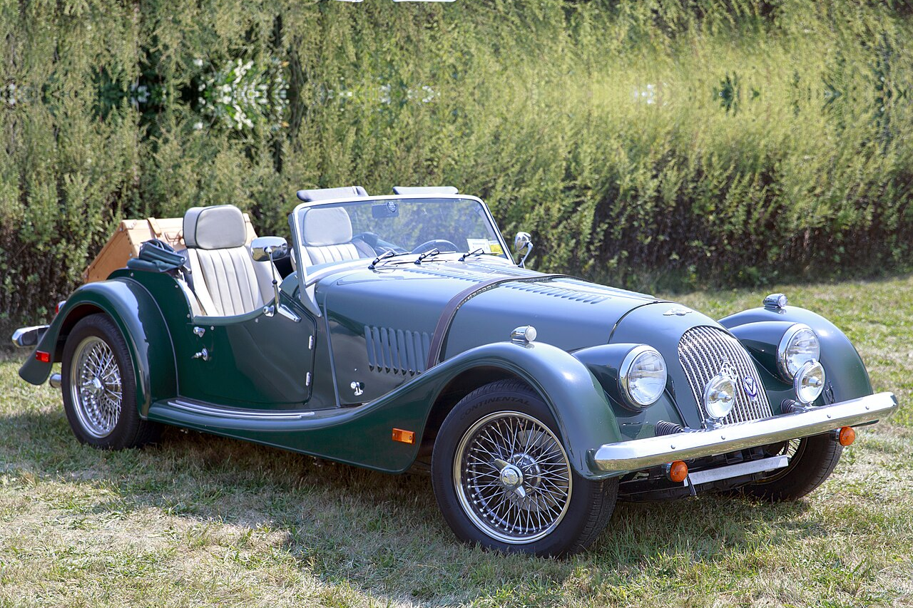 Morgan Plus 8 in British Racing Green, front three-quarter view on grass with wire wheels, chrome grille and twin sidemount headlamps.