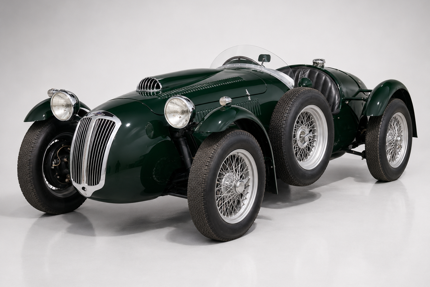 Dark green post-war Frazer Nash Le Mans Replica two-seat sports-racer in a plain studio setting, front three-quarter view showing the tall vertical grille, freestanding round headlamps, cycle-style front wings, aero screen and wire wheels.