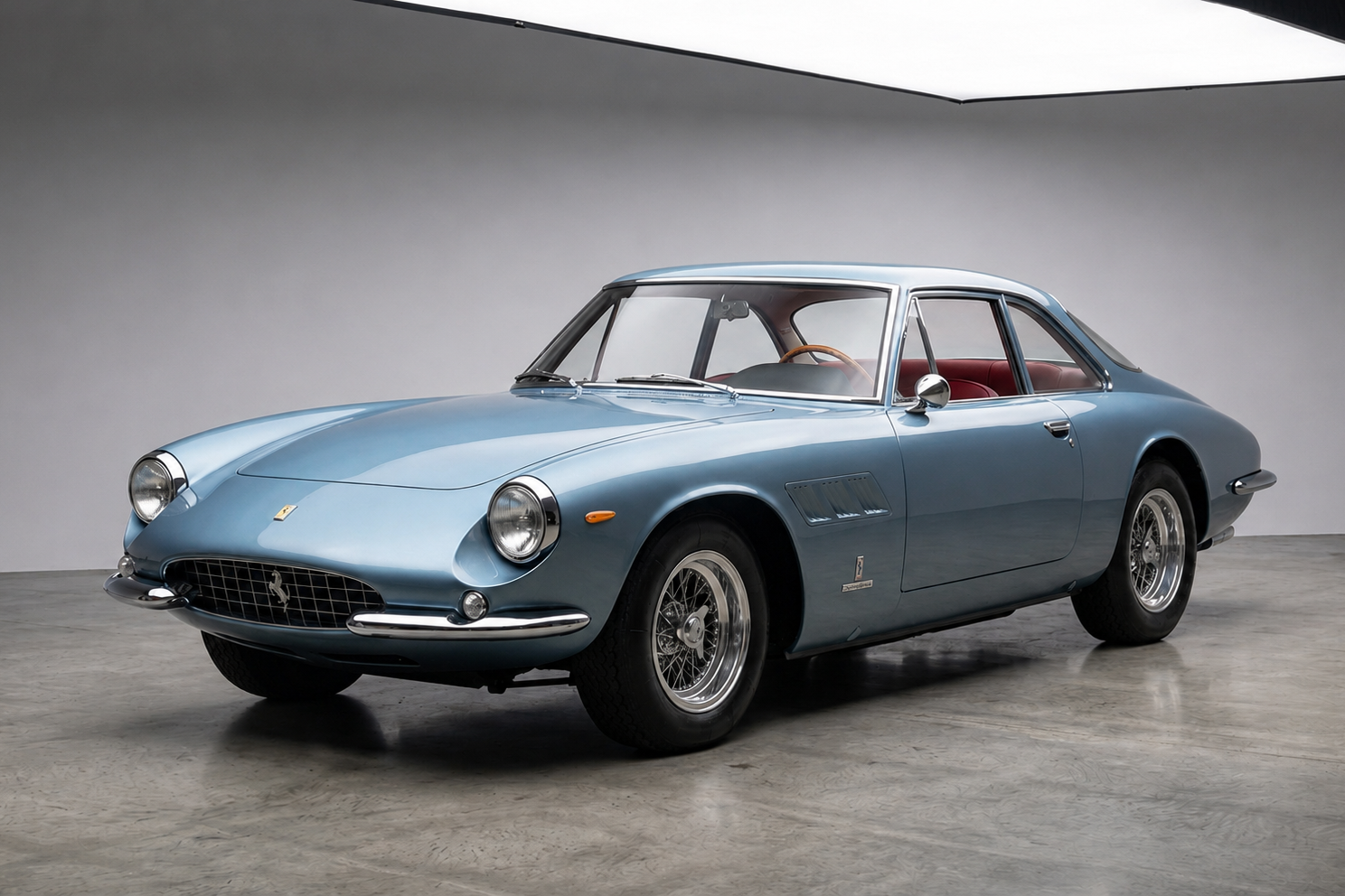 Ferrari 500 Superfast, front three-quarter view — Pininfarina-designed 1964–1966 front-engined V12 Maranello flagship grand tourer in light metallic blue over red leather, exposed round headlamps, chrome bumper and chrome wire wheels, photographed in a plain studio with a polished concrete floor.