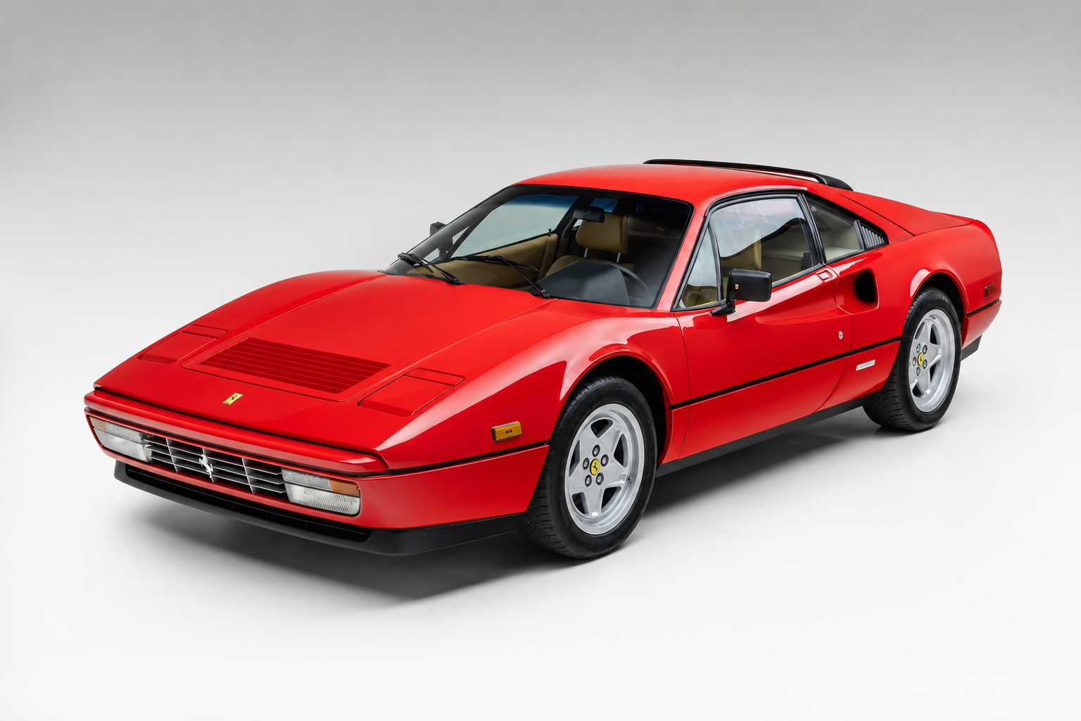 Red Ferrari 328 GTB in a studio setting on a pale grey backdrop, front three-quarter view showing the fixed-roof coupe body, body-coloured bumpers, retracted pop-up headlamps, bonnet vent, side air intake ahead of the rear wheel, convex five-spoke alloy wheels and tan leather interior.