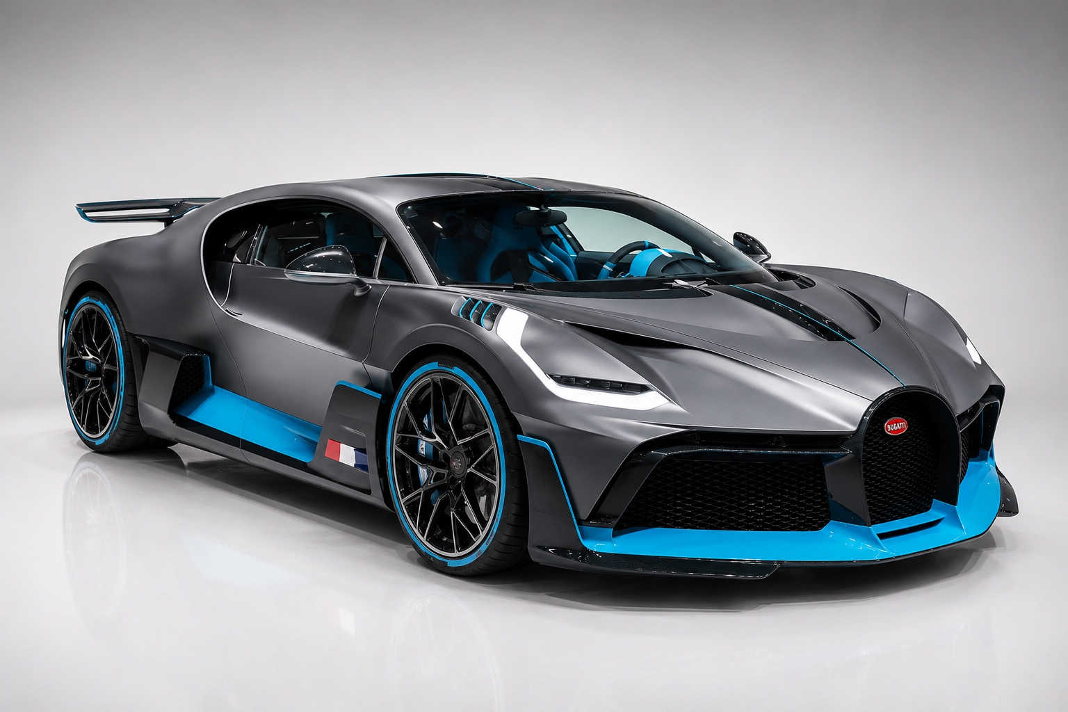 Grey and light blue Bugatti Divo hypercar in a studio setting, front three-quarter view showing the enlarged horseshoe grille, aggressive splitter, blue wheel accents, aerodynamic side blades and the fixed rear wing.