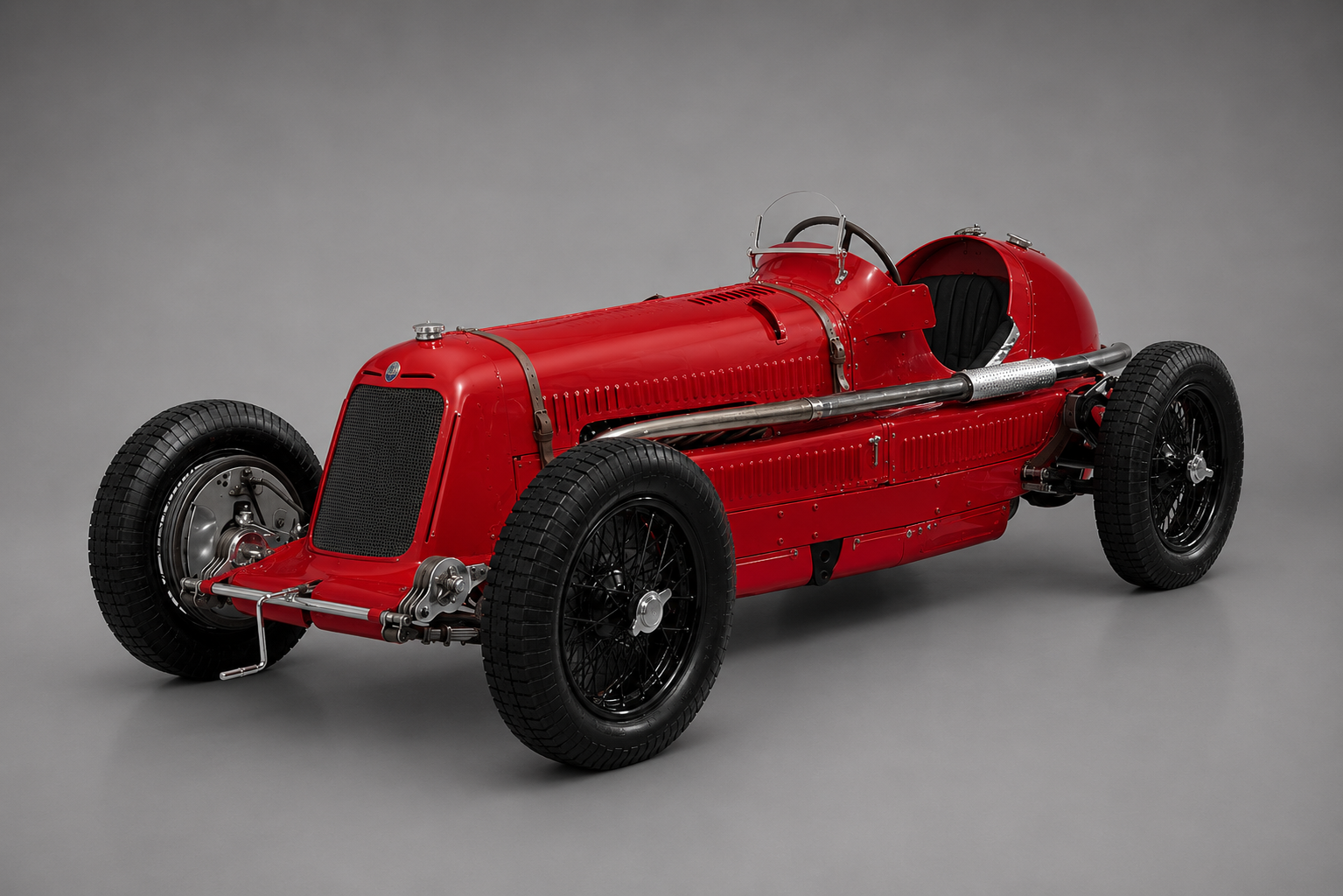 Red pre-war Maserati 8CM / 8CTF monoposto Grand Prix car in a studio setting, front three-quarter view showing the long louvered bonnet, exposed single-seat cockpit with small aero screen, external side exhaust, black wire wheels and mesh grille.