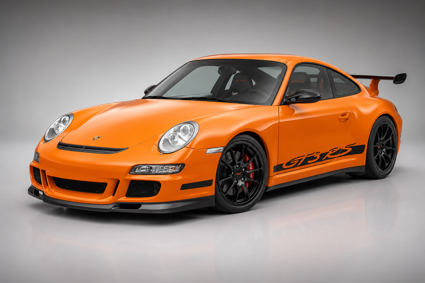 Orange Porsche 911 GT3 RS (997) in a grey studio, front three-quarter view showing the black GT3 RS side script, gloss-black centre-lock wheels and adjustable carbon rear wing.