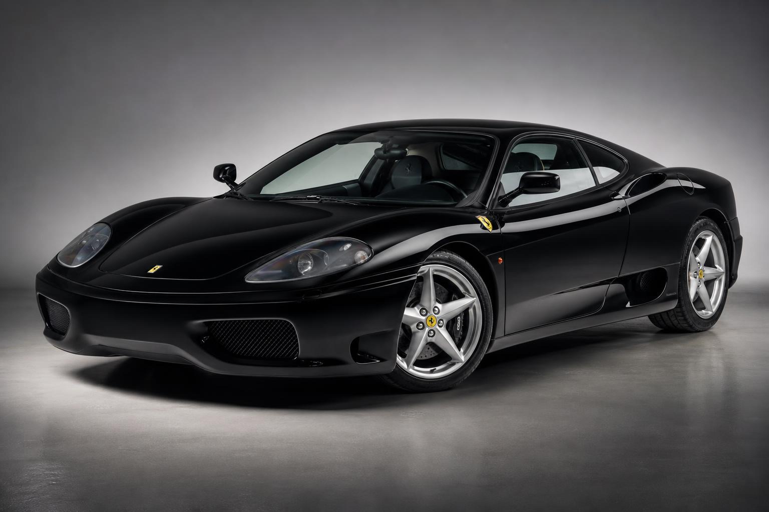 Silver Ferrari 360 Modena coupe, three-quarter view showing the aluminium-spaceframe mid-engined bodywork, twin oval tailpipes, five-spoke alloy wheels and the exposed V8 under the rear glass.