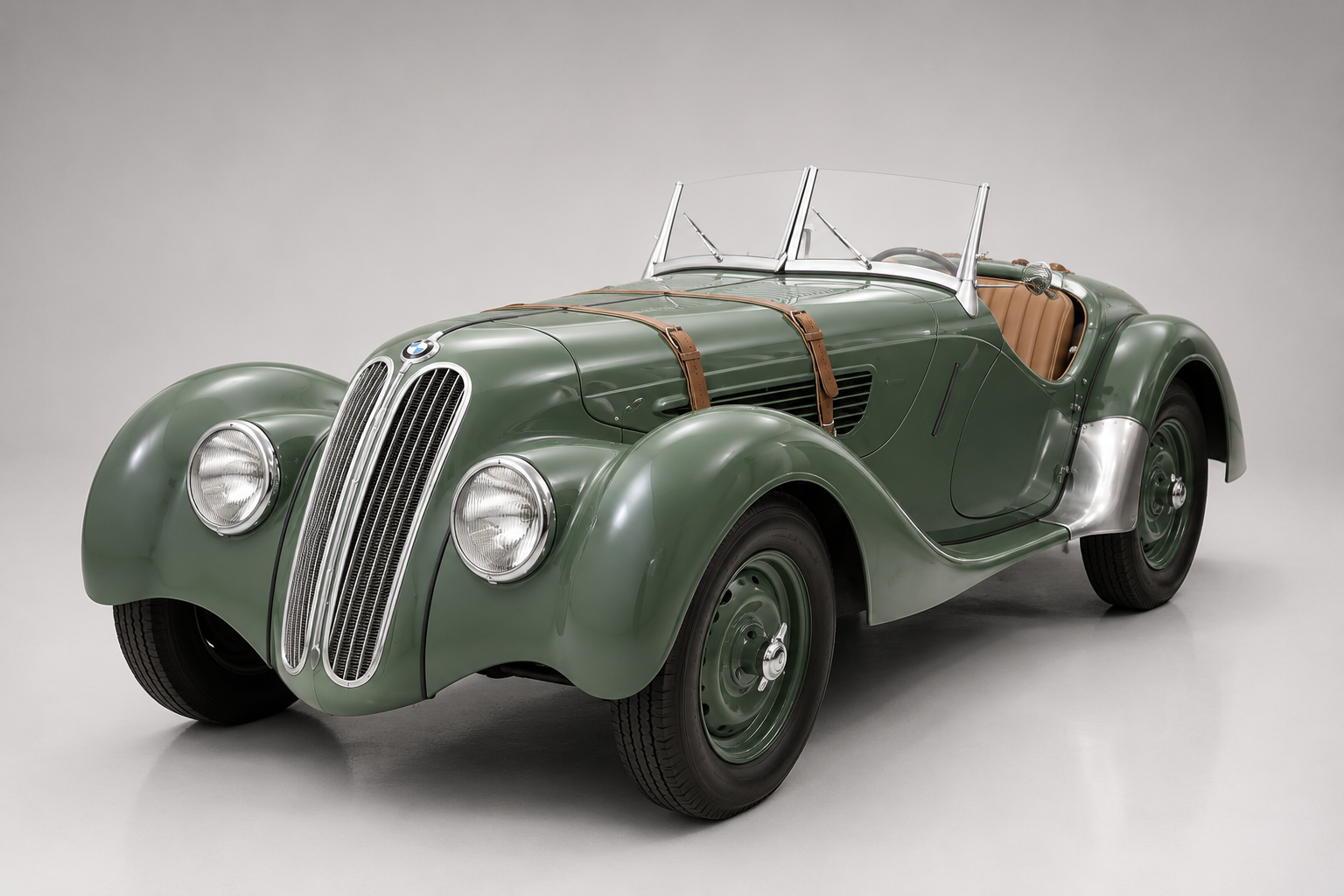 Green BMW 328 roadster in a studio setting, front three-quarter view showing the twin-kidney chrome grille, freestanding headlamps, leather bonnet straps, tan interior and body-coloured steel wheels.