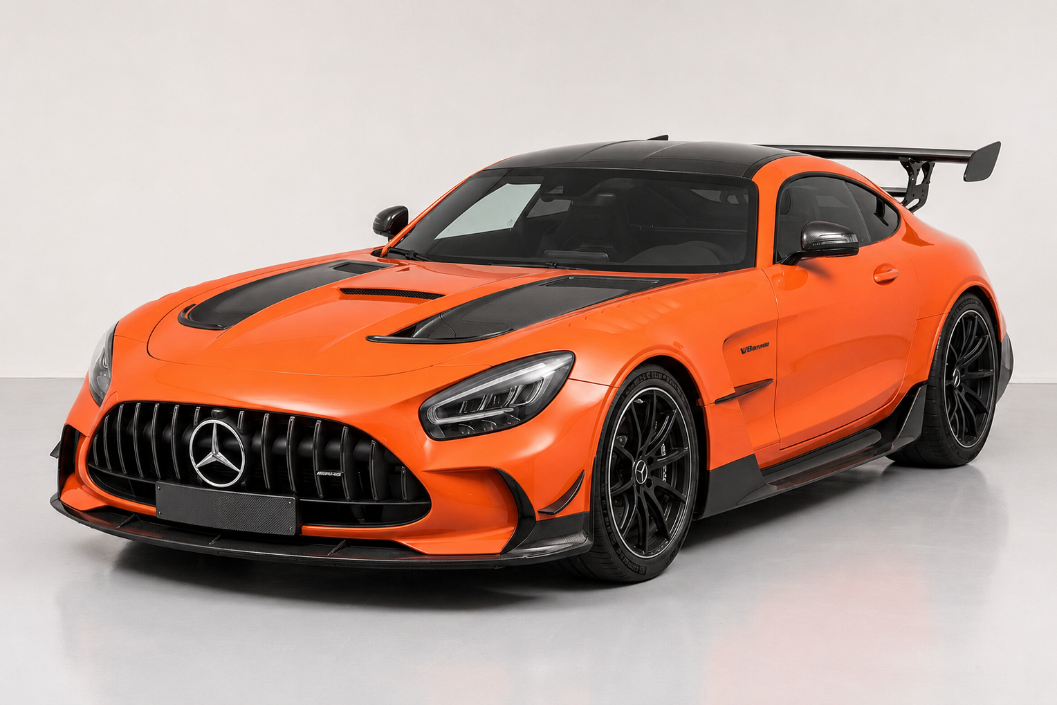 Orange Mercedes-AMG GT Black Series (C190) with black carbon roof, bonnet vents and large fixed rear wing, front three-quarter view in a studio against a neutral background, showing the wide Panamericana grille, front splitter and black forged wheels.