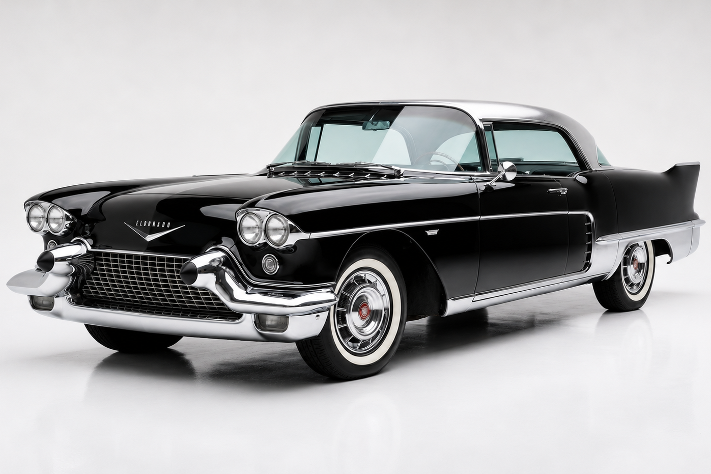Black 1957 Cadillac Eldorado Brougham four-door hardtop in a bright studio, front three-quarter view showing the brushed stainless-steel roof, twin sets of headlamps (quad headlamps in period), heavy chrome front bumper with bullet overriders, chrome-trimmed body sides, whitewall tyres on chrome hubcaps and a low, formal profile.