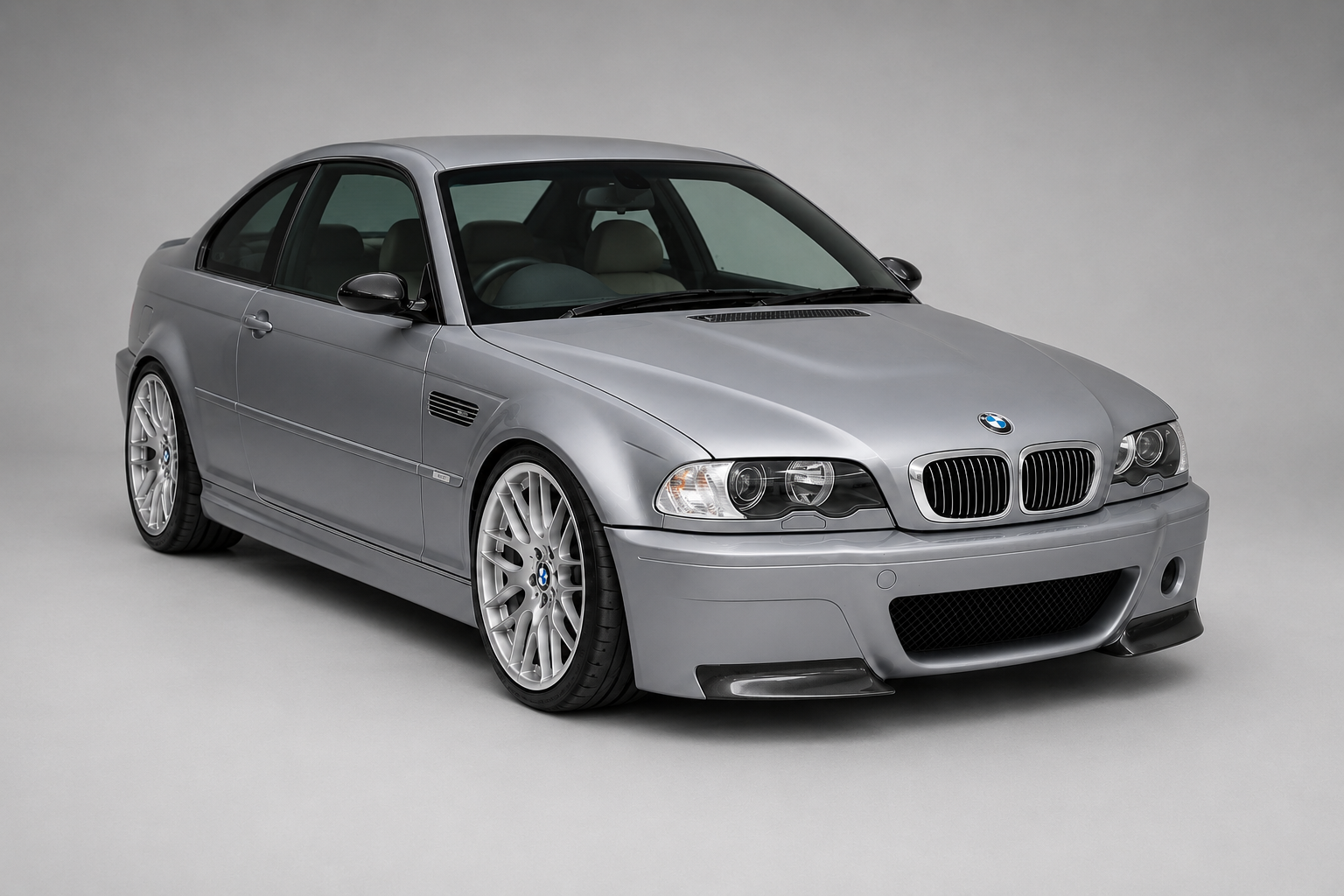 Silver BMW M3 (E46) coupe in a grey studio setting, front three-quarter view showing the twin kidney grille, xenon headlamps, front side gill vent, front splitter and multi-spoke silver alloy wheels.