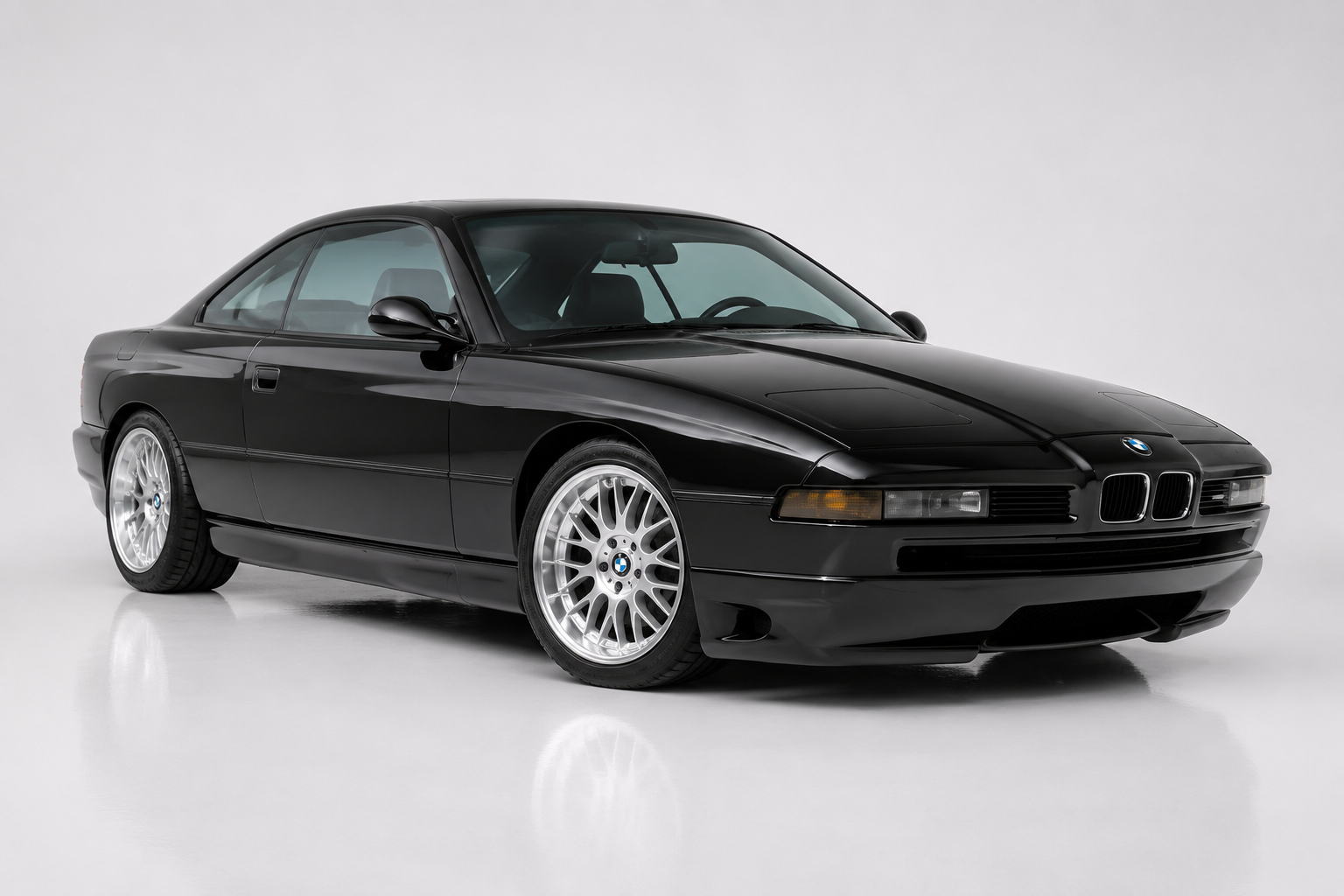 Black BMW 8 Series (E31) two-door coupé, front three-quarter view in a studio, showing the low pop-up-headlamp nose, the kidney grille flanked by amber indicators, pillarless side glass and multi-spoke alloy wheels.