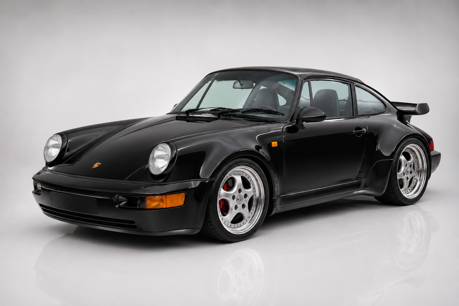 Black Porsche 911 Turbo (964) in a studio, front three-quarter view showing the wide riveted rear arches, tea-tray rear wing and polished Cup-style wheels.