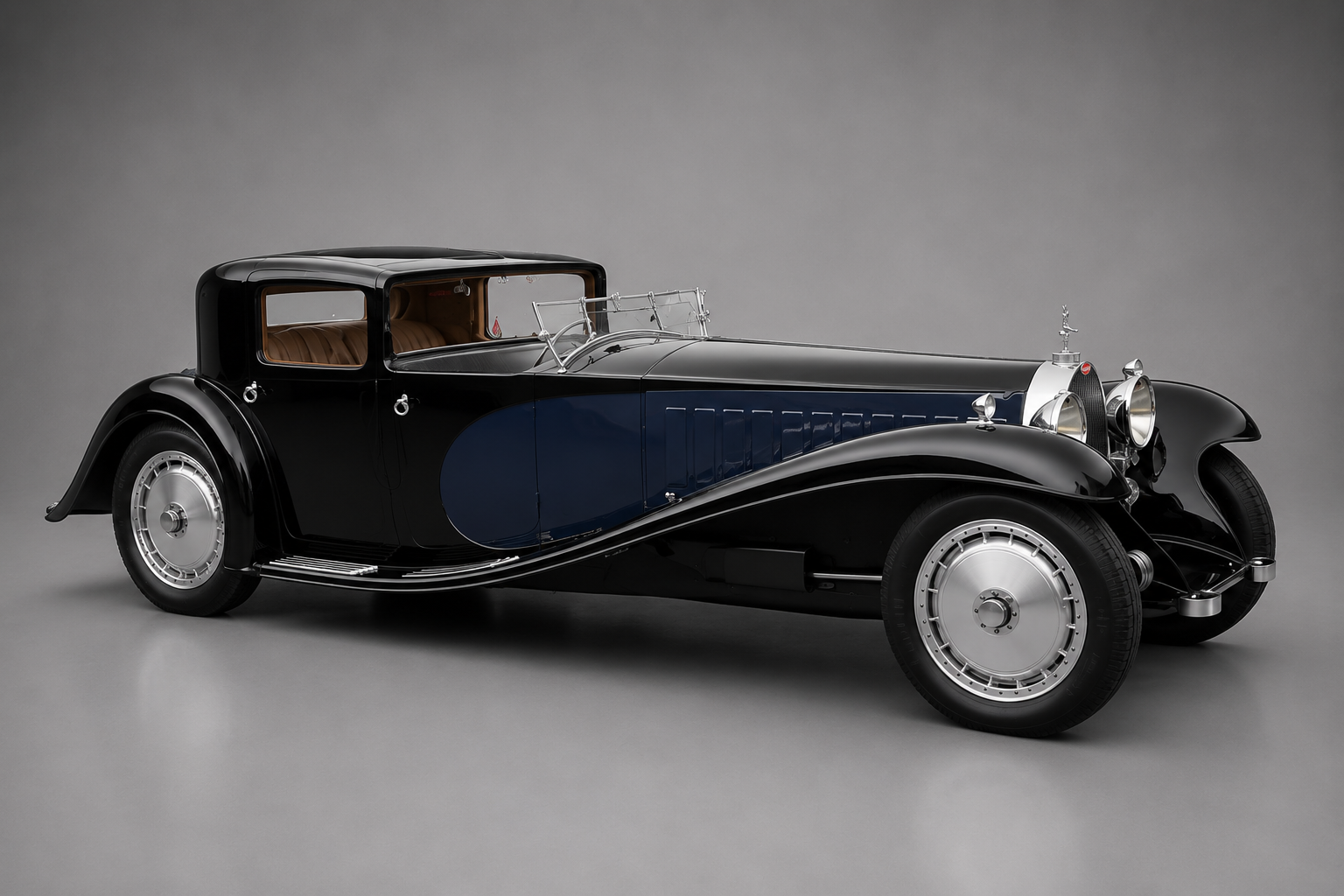 Black and dark blue Bugatti Type 41 Royale Coupé de Ville with tan leather rear compartment, side three-quarter studio view on a grey backdrop showing the elephant mascot, tall chrome horseshoe radiator, sweeping front wings and polished disc wheels.