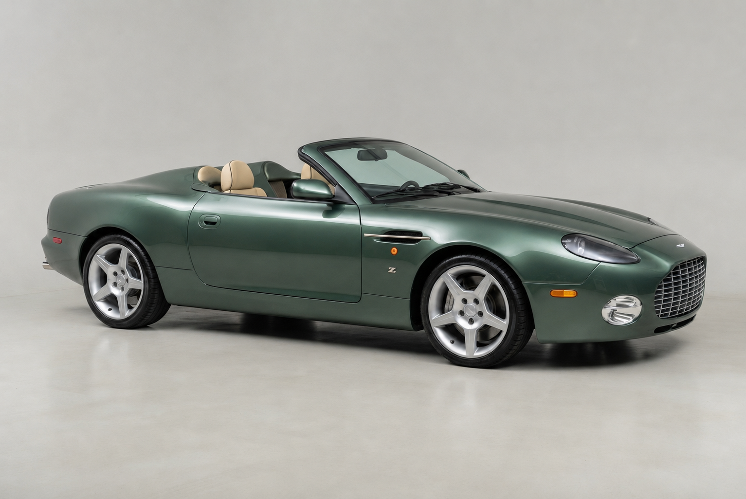 Green Aston Martin DB AR1 roadster with a tan leather interior and the roof folded, side-profile studio view on a pale grey background, showing the long bonnet, swage line, five-spoke alloy wheels and Zagato Z badge.