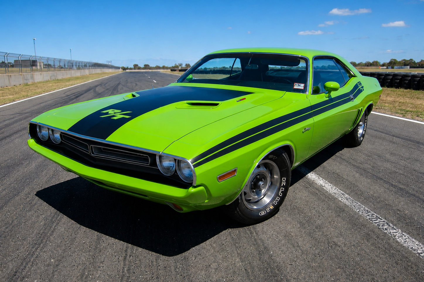 Dodge Challenger R/T in bright Sublime green with matte-black hood stripes and R/T graphic, twin bonnet scoops and black steel wheels, front three-quarter view on an empty racetrack straight — the E-body Mopar pony car in a signature factory colour.