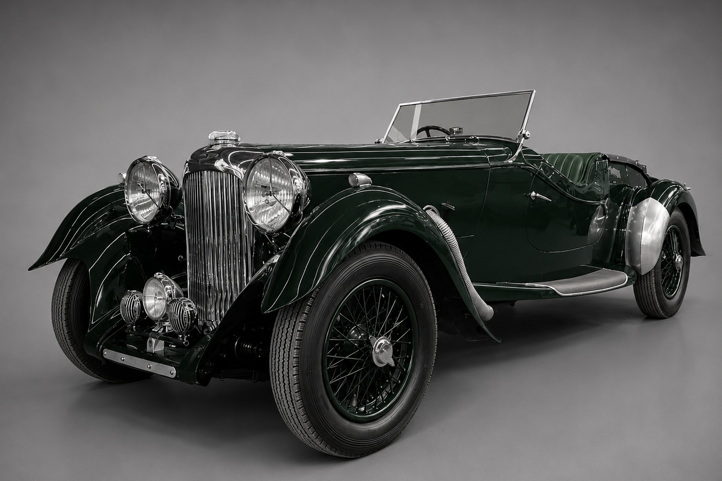 Dark green pre-war Lagonda LG45 / V12 open tourer with polished aluminium bonnet-side panel, front three-quarter studio view on a plain grey backdrop showing the tall chrome radiator, twin headlamps, sweeping front wings and black wire wheels.