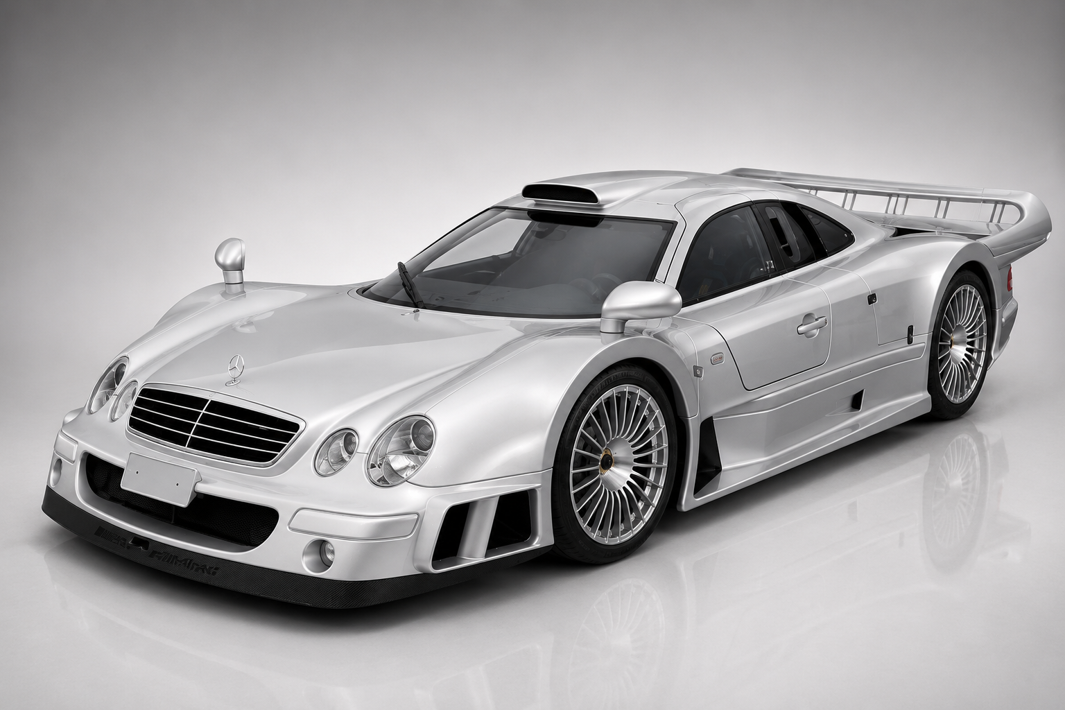 Silver Mercedes-Benz CLK GTR Straßenversion in a studio setting, front three-quarter view showing the FIA GT1 homologation bodywork, dramatic rear wing, carbon-fibre monocoque proportions, roof-mounted air intake, multi-spoke alloy wheels and the mid-mounted V12 cooling vents.