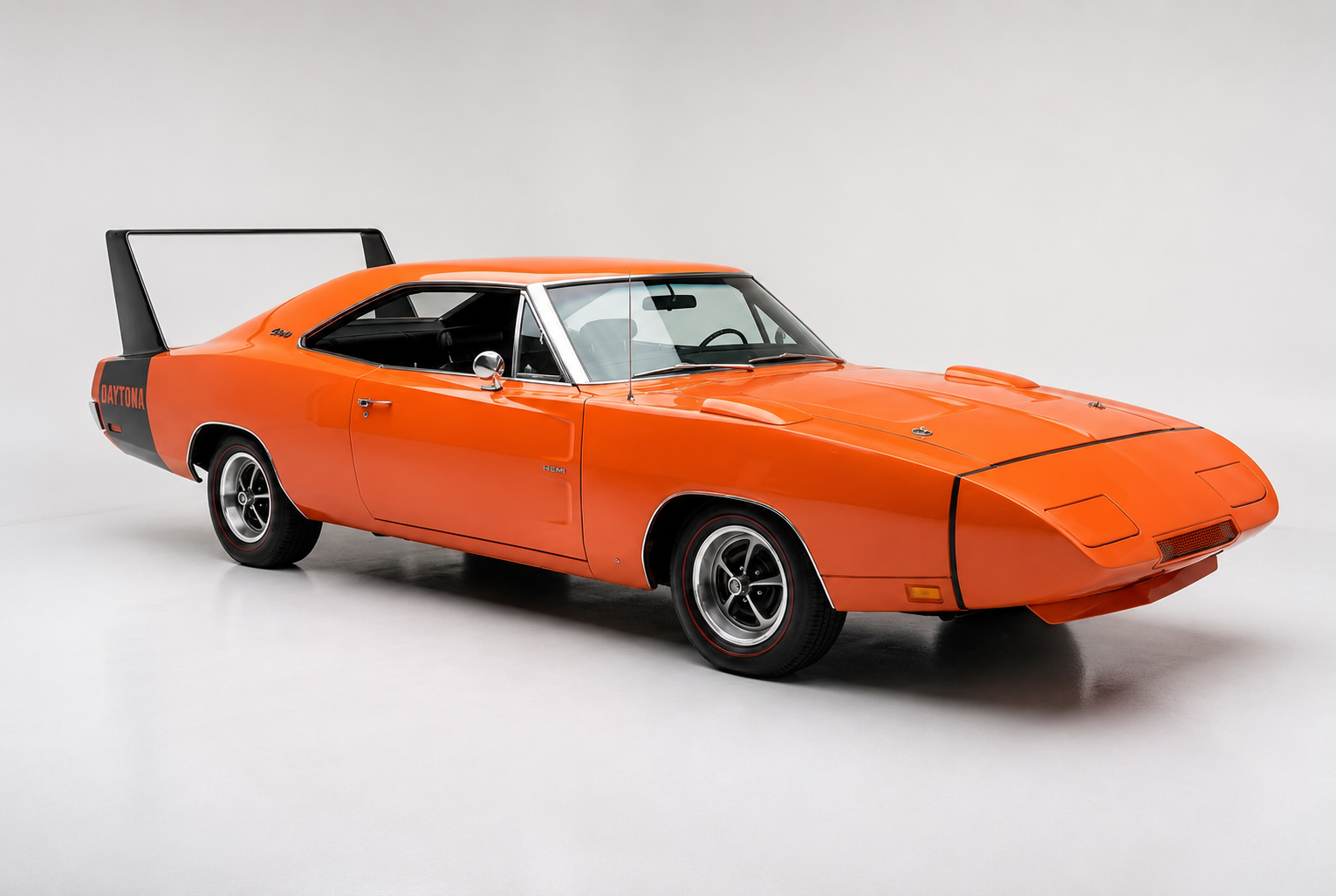 Dodge Charger Daytona, front three-quarter view — a bright orange 1969 winged NASCAR-homologation Mopar coupé with an extended pointed nose cone, pop-up headlamps, black rear quarter panel with 'DAYTONA' script, the signature towering rear wing on twin uprights and black five-spoke wheels, photographed in a plain pale grey studio.