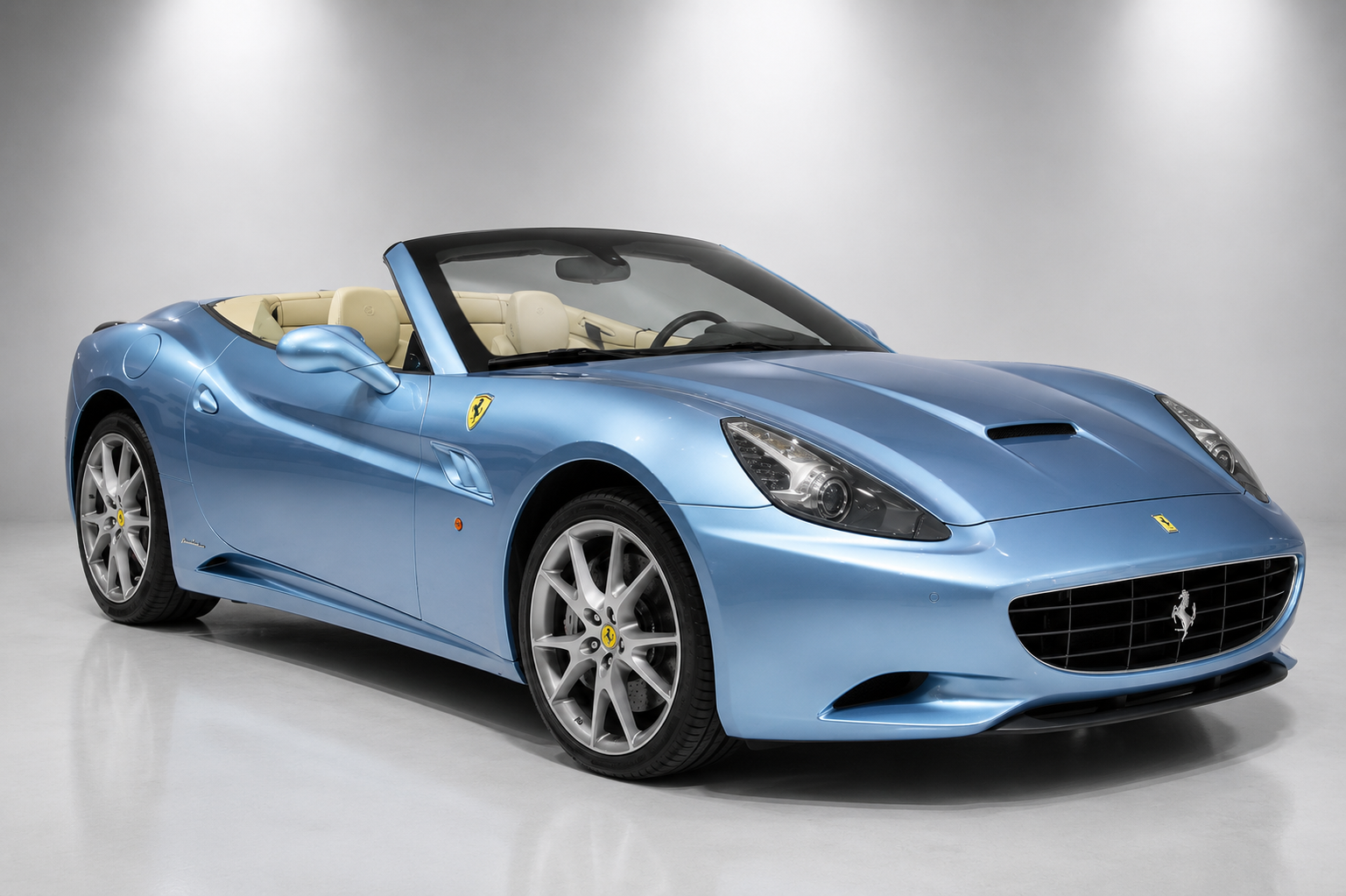 Light blue Ferrari California convertible with the folding hardtop down, cream leather interior, and silver alloy wheels, in a studio setting.