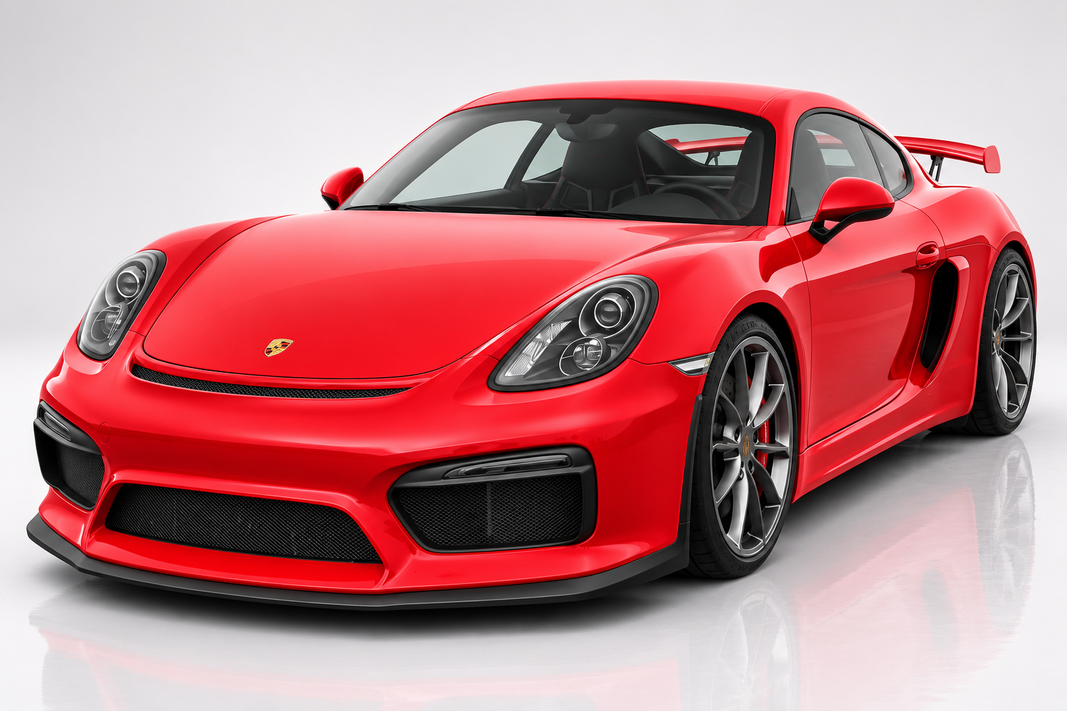 Red Porsche Cayman GT4 in a studio setting, front three-quarter view showing the fixed rear wing, GT4-specific front bumper with central splitter, side intakes and dark five-spoke alloy wheels.