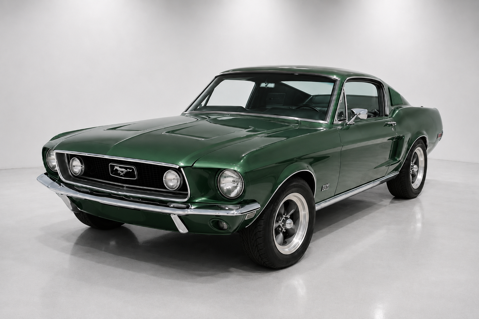 Green 1967 Ford Mustang GT fastback in a studio setting, showing the chrome grille with running-horse badge, quad headlights, GT side badge and silver wheels with white-wall tyres.