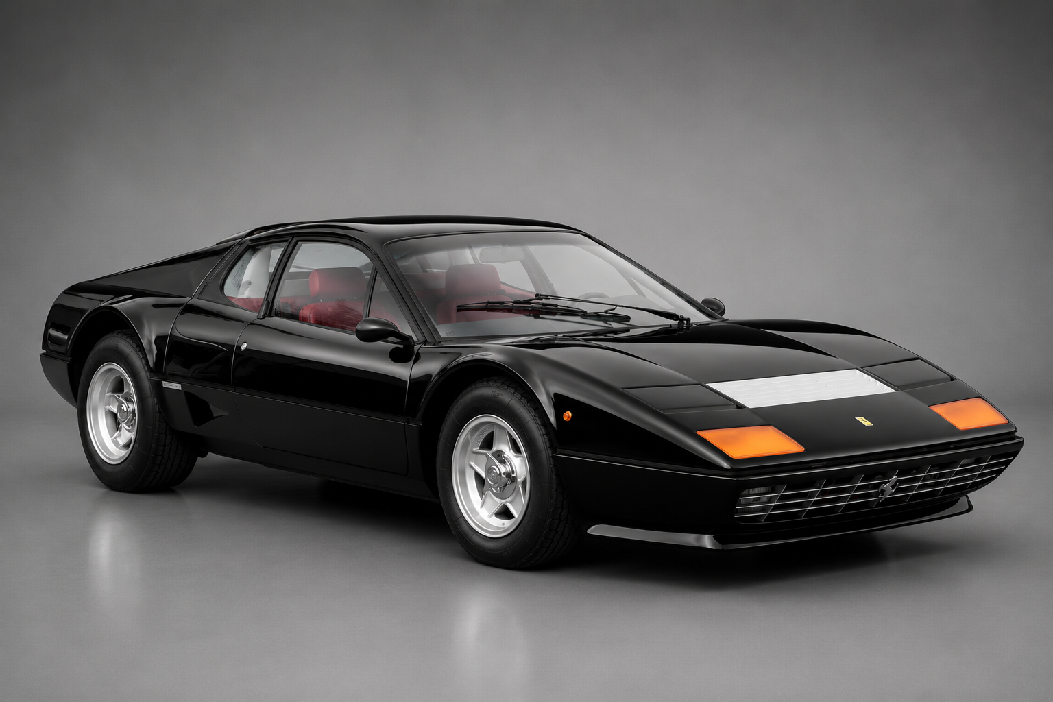 Black Ferrari 512 BB Berlinetta Boxer in a studio setting on a grey backdrop, front three-quarter view showing the Pininfarina wedge profile, amber front indicators, five-spoke alloy wheels and red leather interior.
