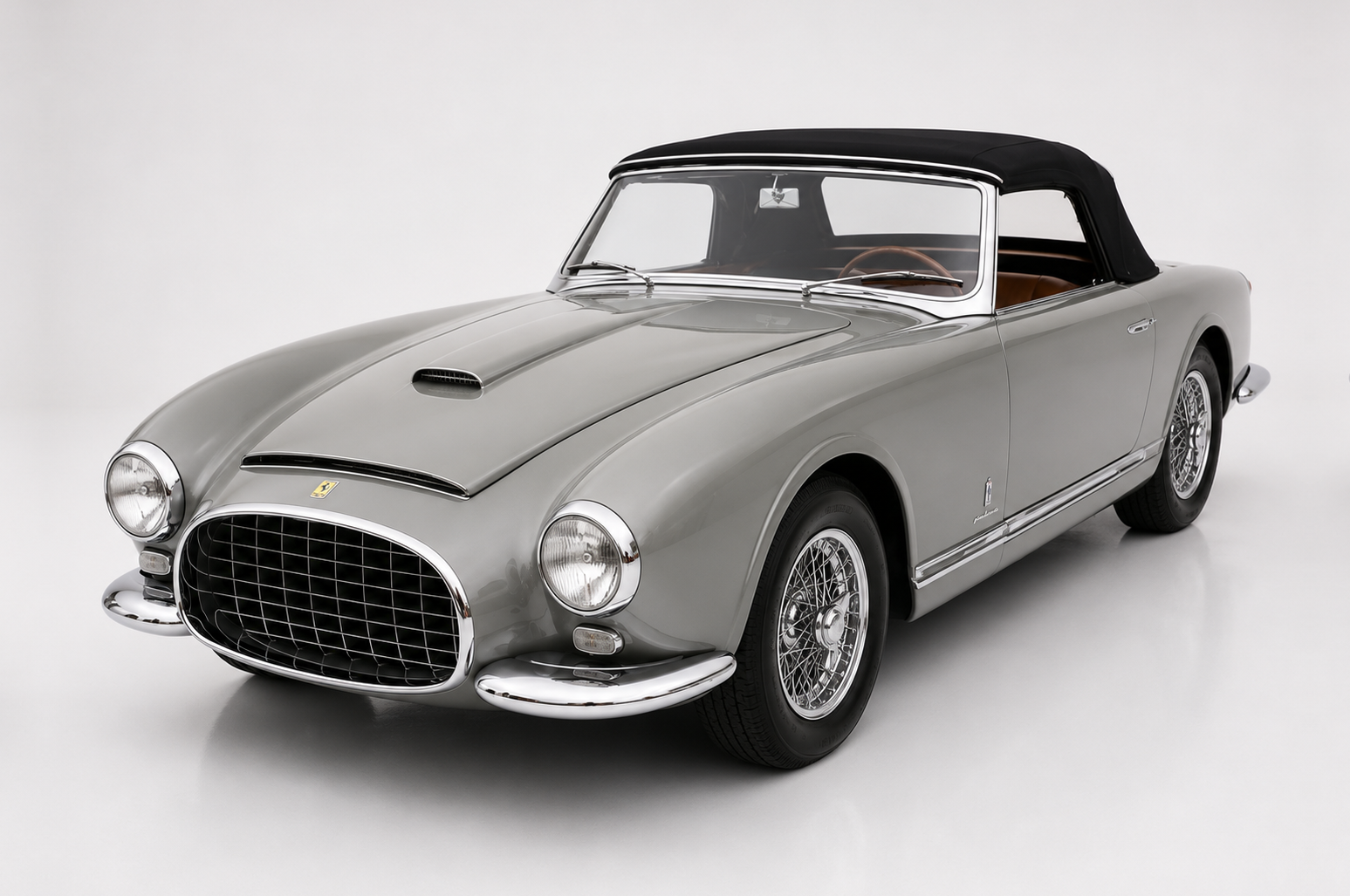 Silver Ferrari 342 America Pinin Farina cabriolet photographed in a studio with a black soft top raised, front three-quarter view showing the tall mesh grille, chrome bumper, bonnet scoop, faired-in headlamps and centre-lock wire wheels.
