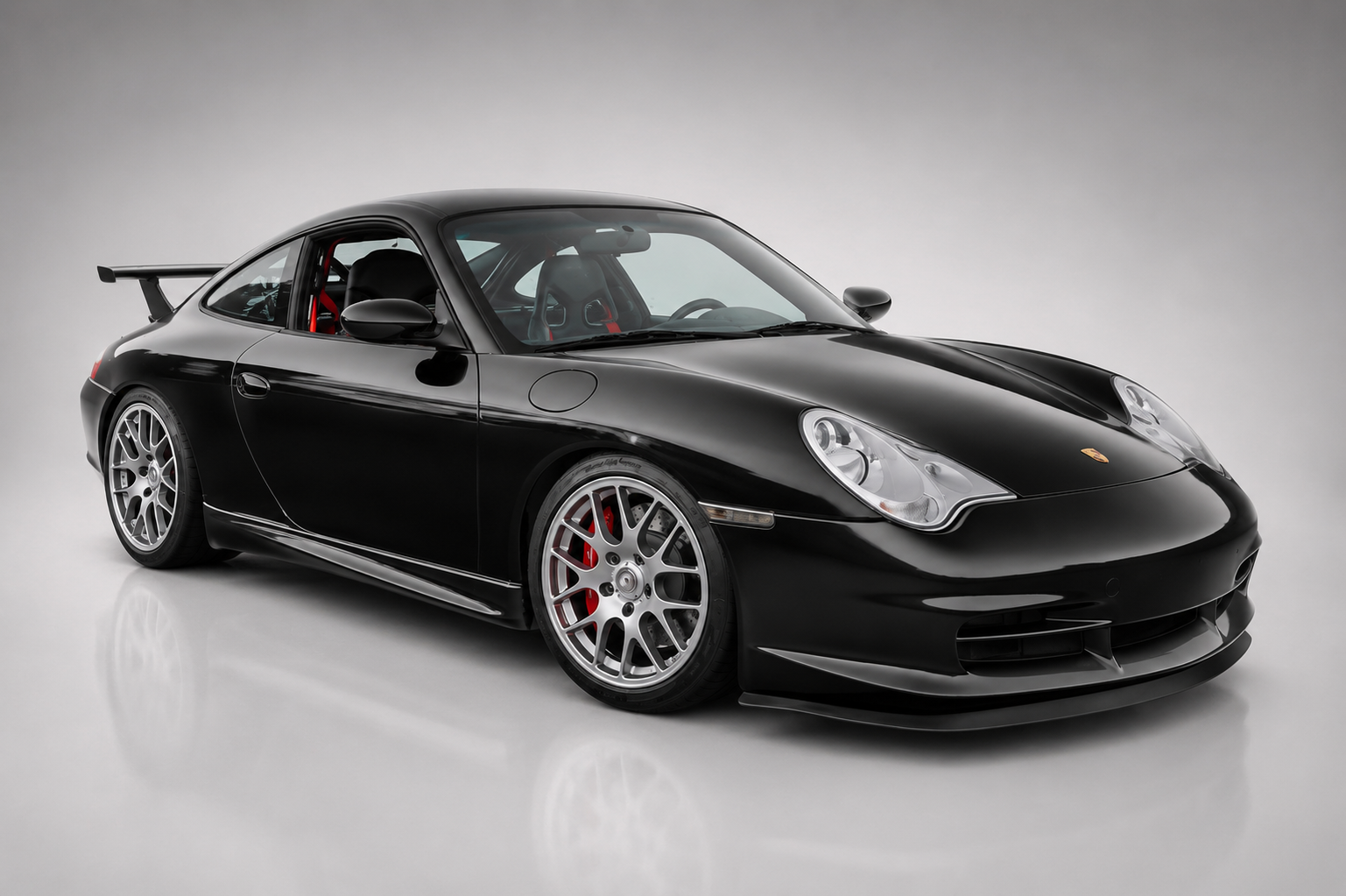 Porsche 911 GT3 (996) in black, front three-quarter studio view showing the fixed rear wing, deep front splitter and silver alloy wheels.