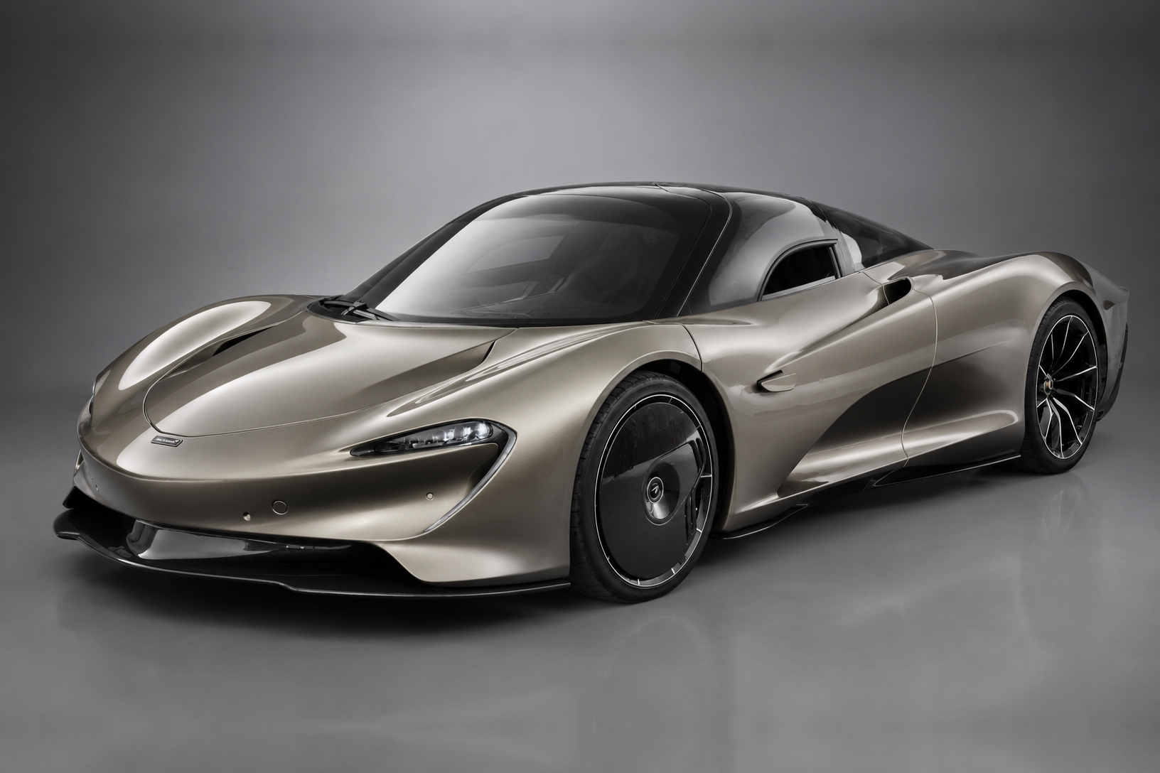 Champagne-silver McLaren Speedtail in a studio setting, front three-quarter view showing the teardrop body, dihedral doors closed and covered rear wheels.