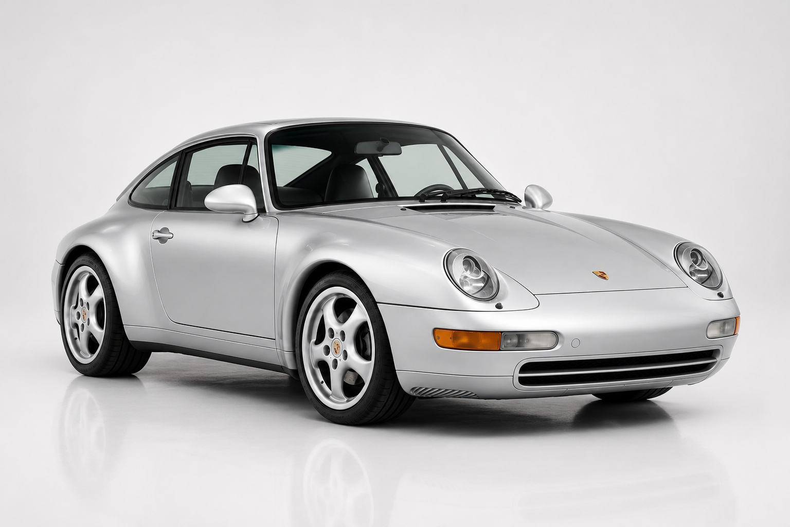 Silver Porsche 911 (993) coupe photographed in a studio, front three-quarter view showing the rounded oval headlamps, integrated bumpers, low nose and factory five-spoke alloy wheels of the last air-cooled 911.