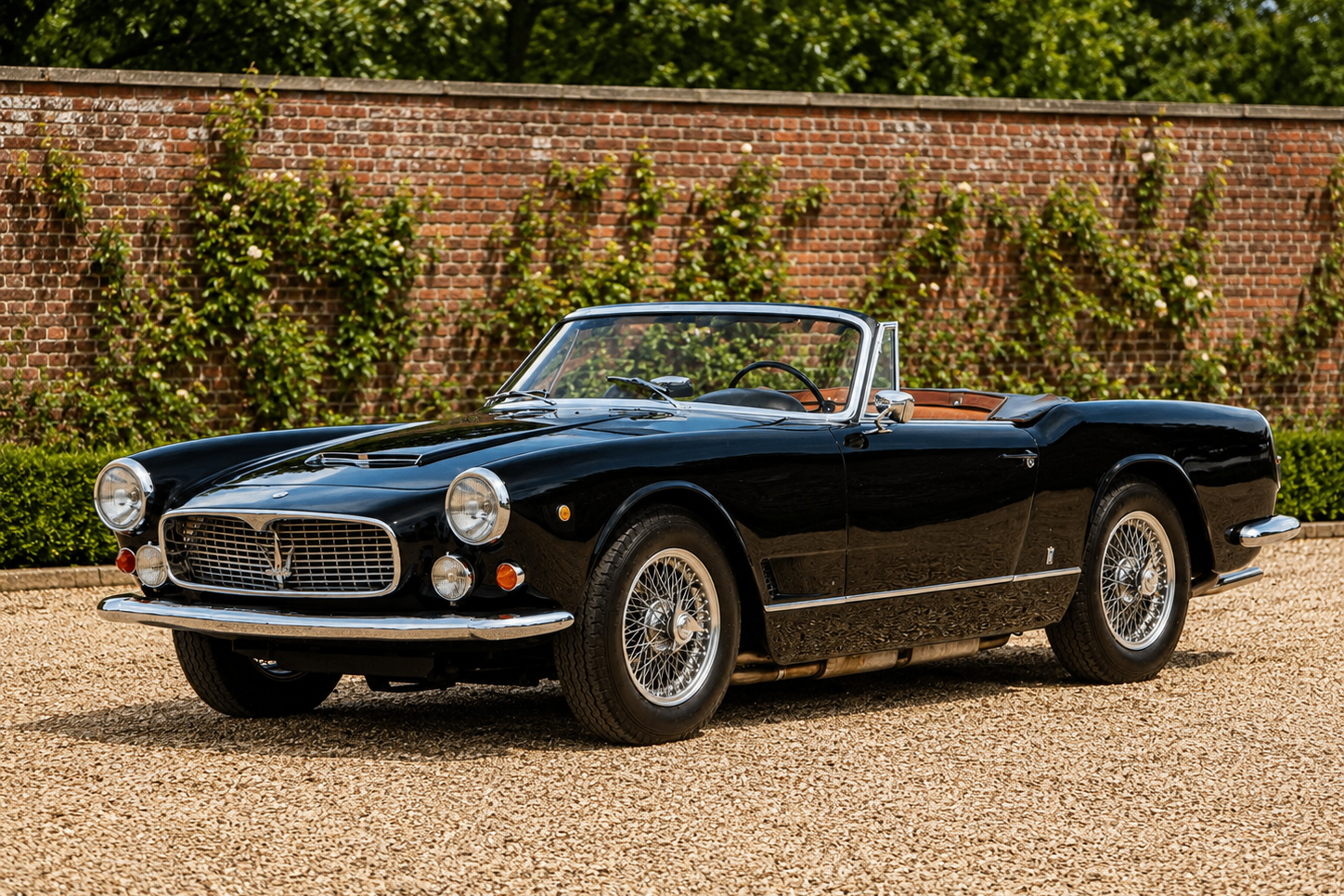 Maserati 3500 GT Spyder by Vignale in black, front three-quarter view on a concours-quality gravel courtyard against a walled garden showing the Michelotti-drawn Vignale Spyder coachwork, oval Trident grille, Borrani wire wheels and tan leather interior of the 1959–1964 open two-seat variant of the 1957–1964 Tipo 101 3500 GT model line.